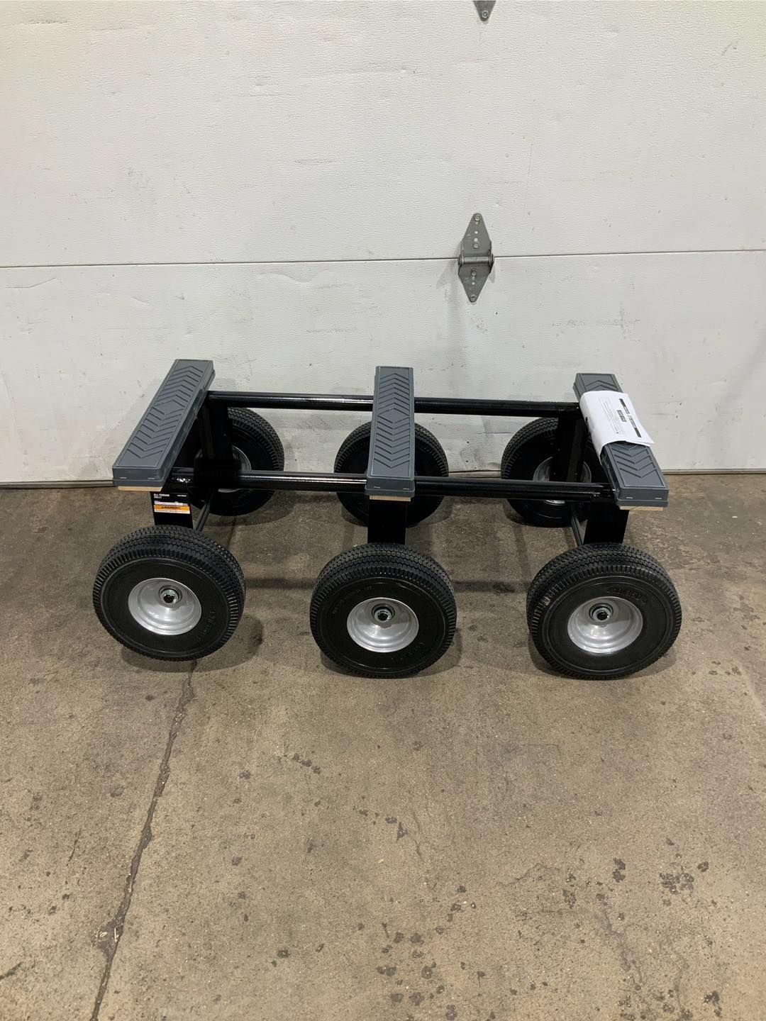 A cart with four wheels is sitting on the ground in front of a garage door.