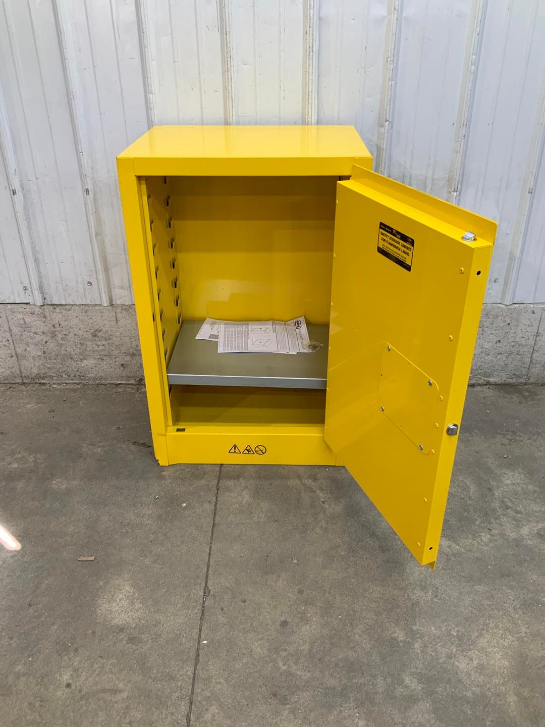 A yellow safety cabinet with the door open and a metal shelf.