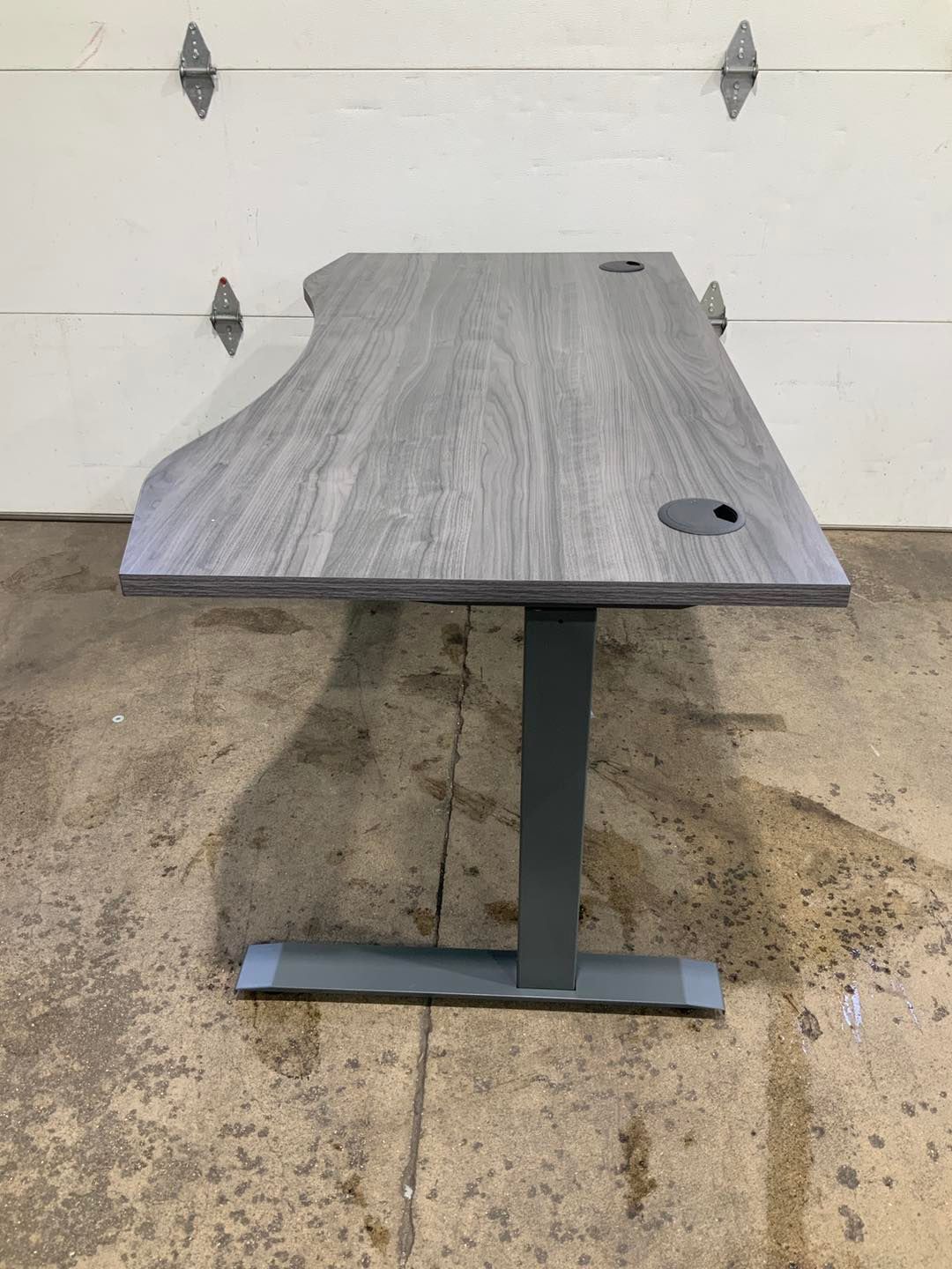 A gray desk is sitting on a concrete floor in front of a garage door.
