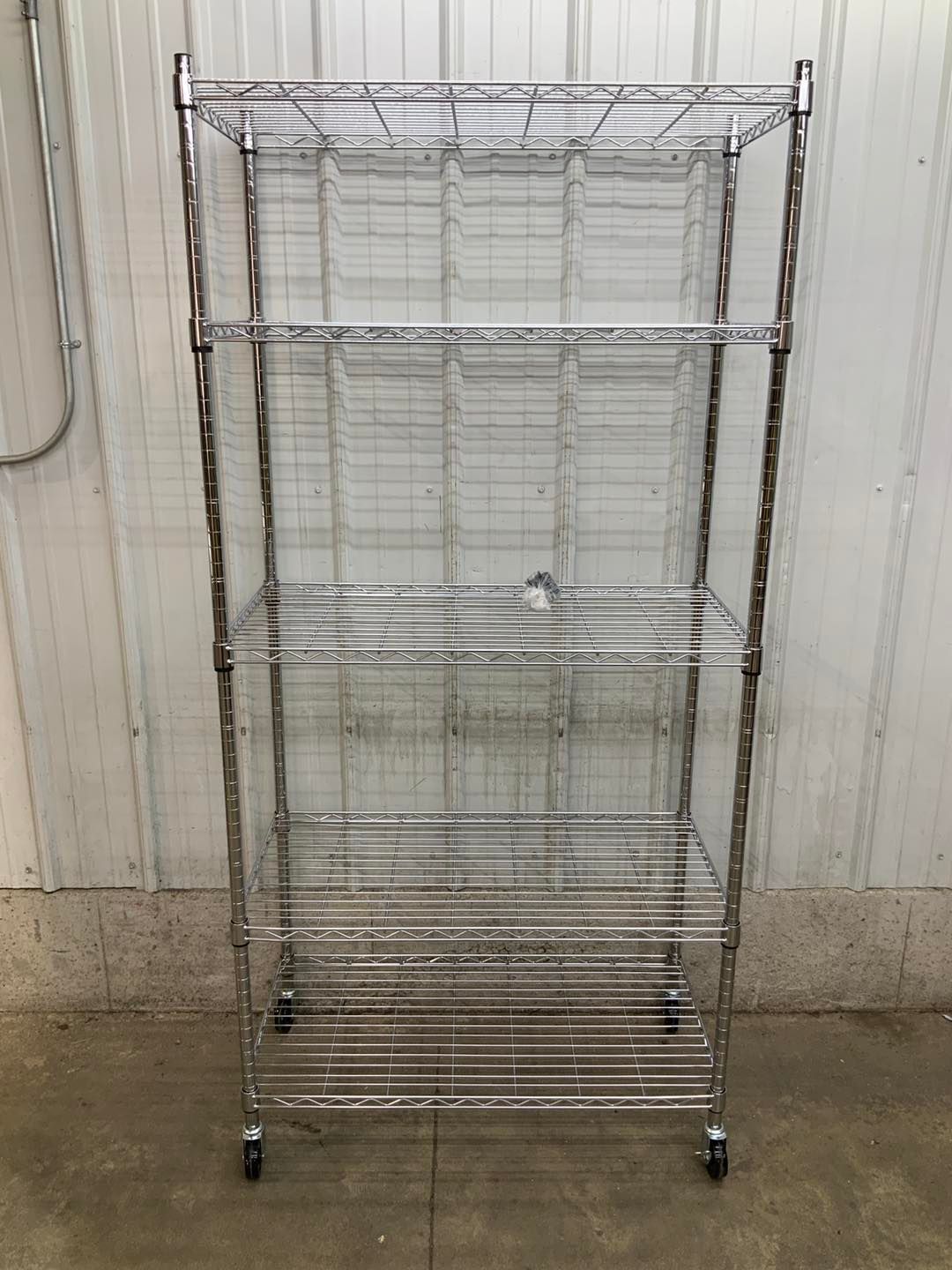 A metal shelf with wheels is sitting in front of a white wall.