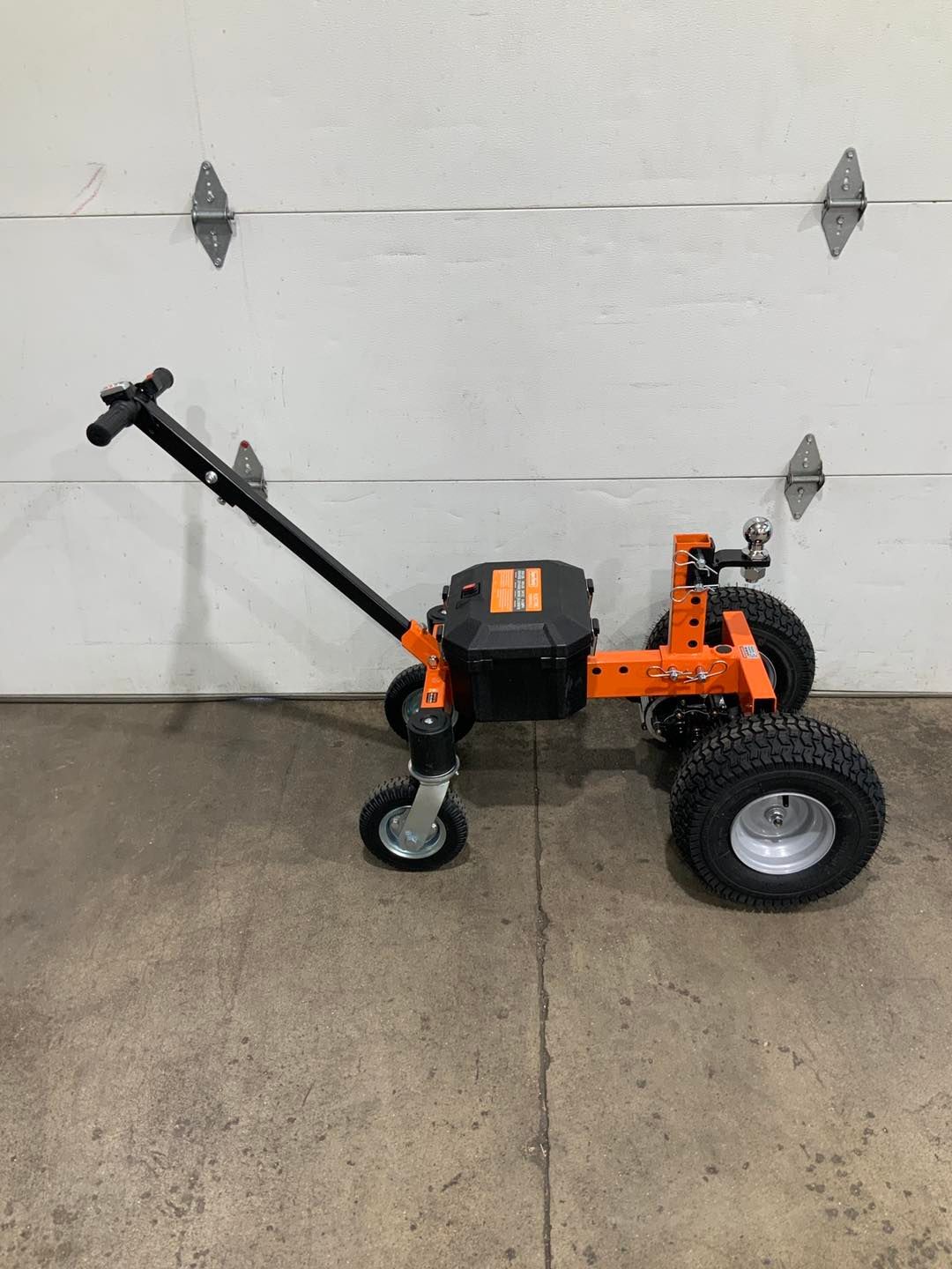 An orange and black lawn mower is parked in front of a garage door.