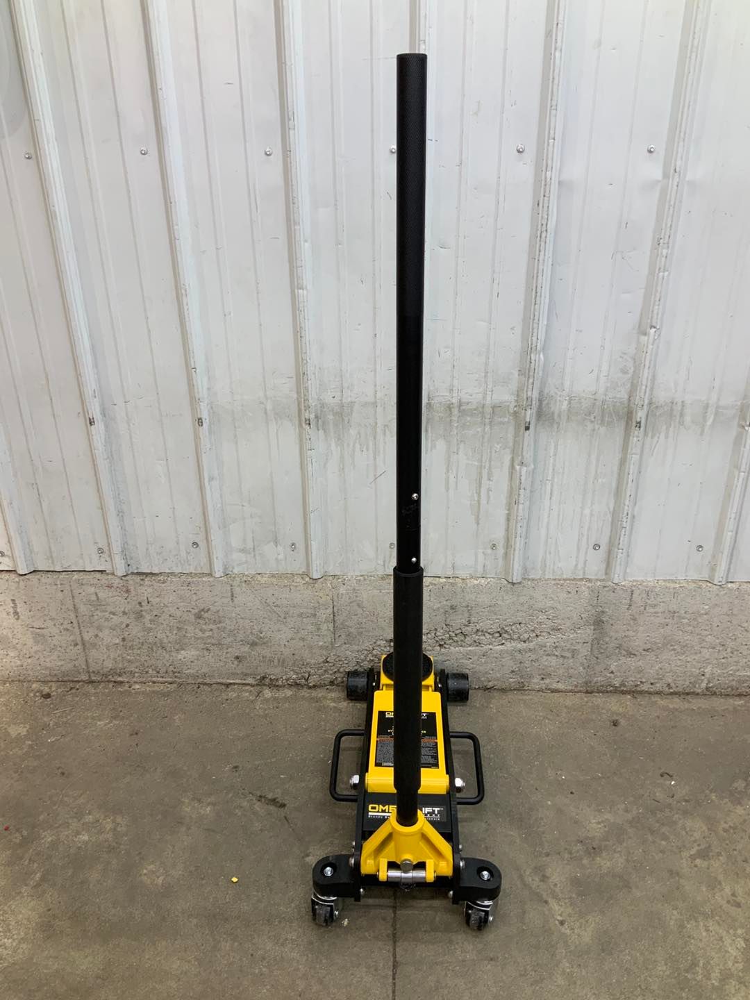 A yellow and black floor jack is sitting on the ground in front of a white building.