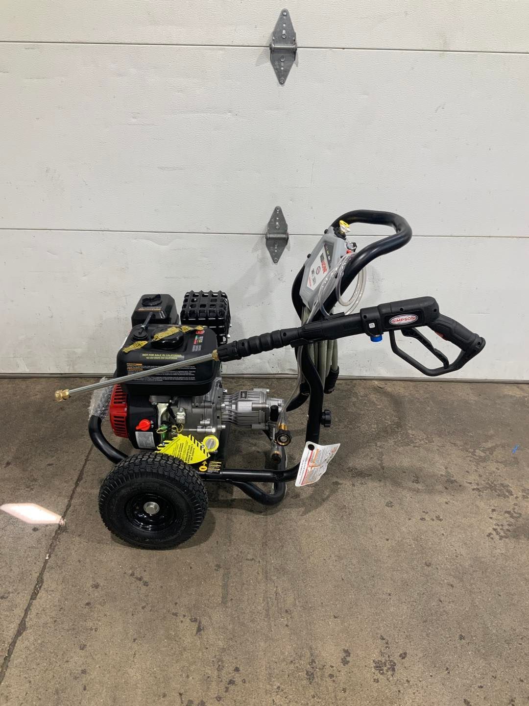 A gas powered pressure washer is sitting in front of a garage door.