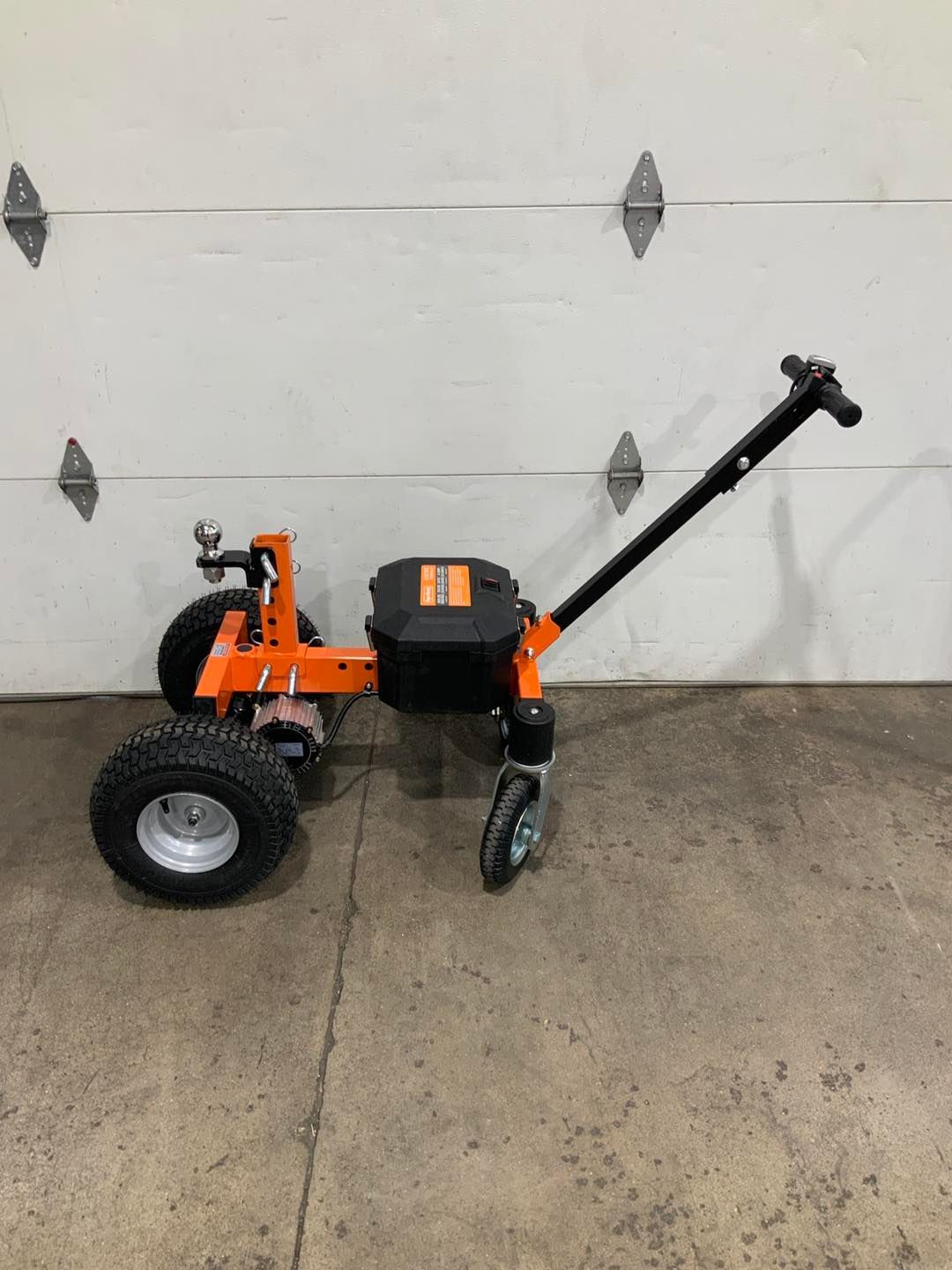 A small orange tractor is parked in front of a garage door.