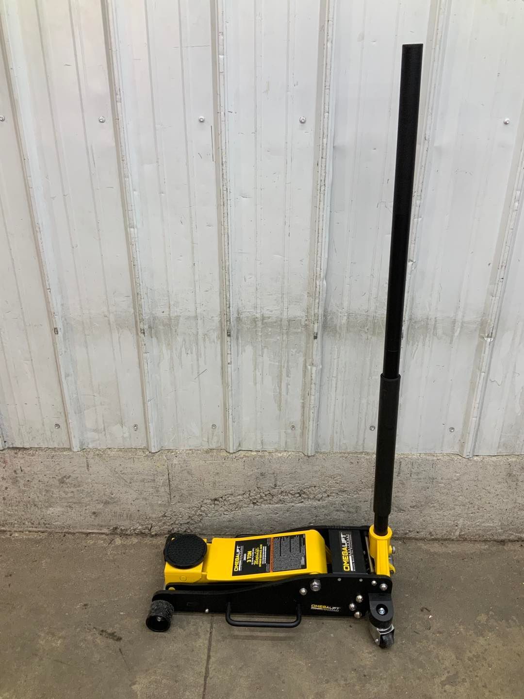 A yellow and black floor jack is sitting on the ground in front of a white wall.