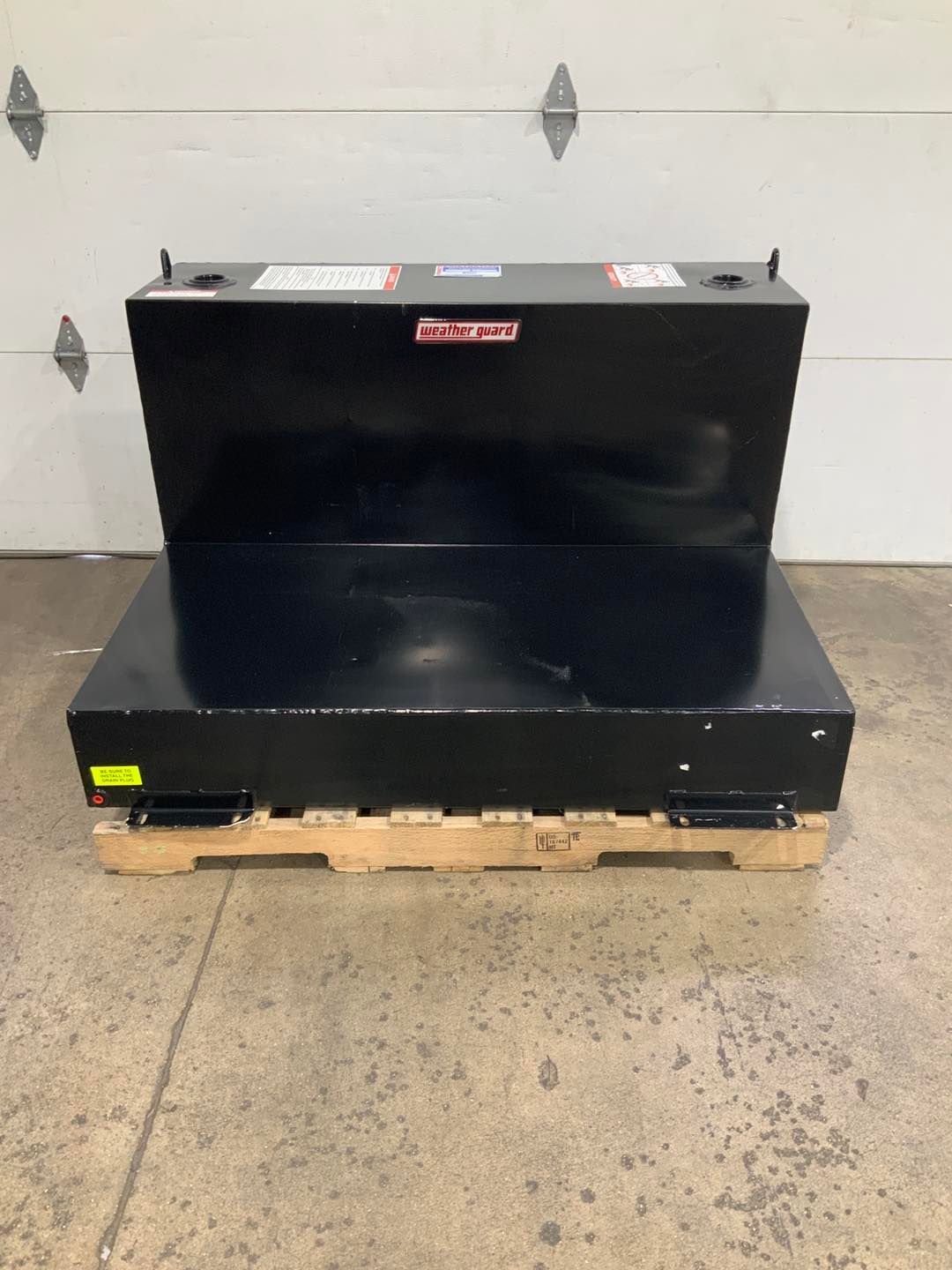 A black tank is sitting on a wooden pallet in front of a garage door.
