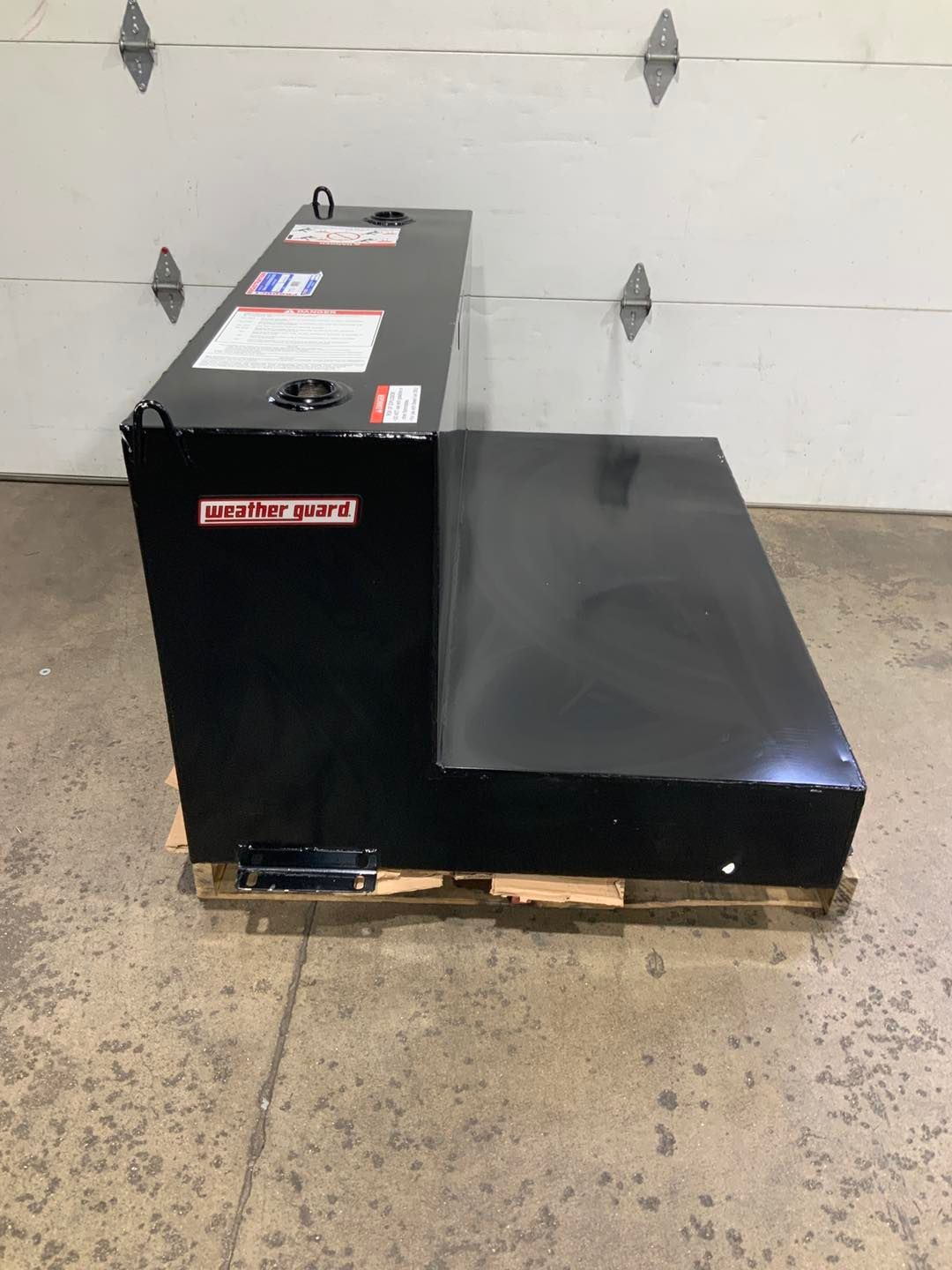 A black tank is sitting on a wooden pallet in front of a garage door.