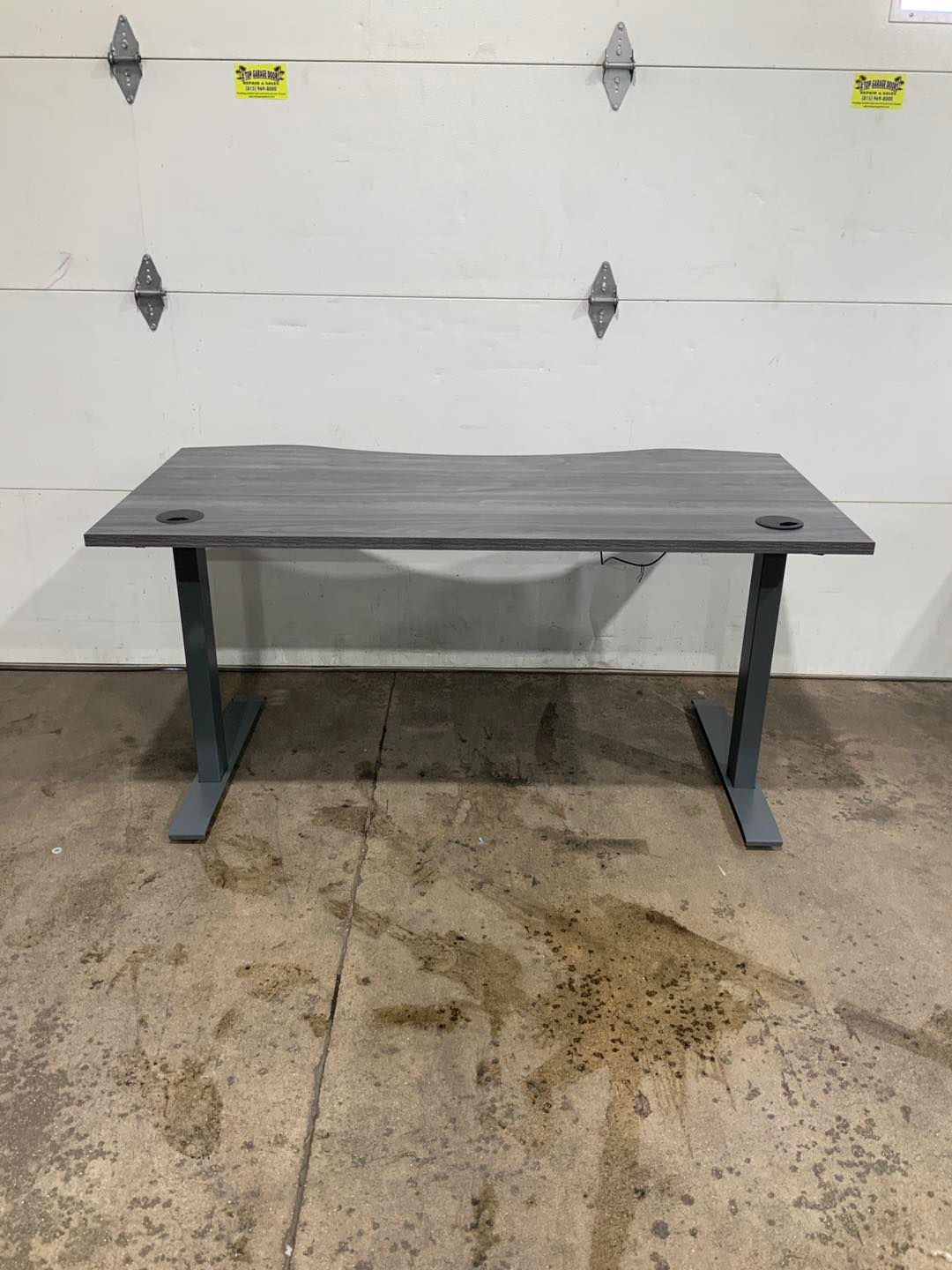A gray standing desk is sitting in front of a garage door.