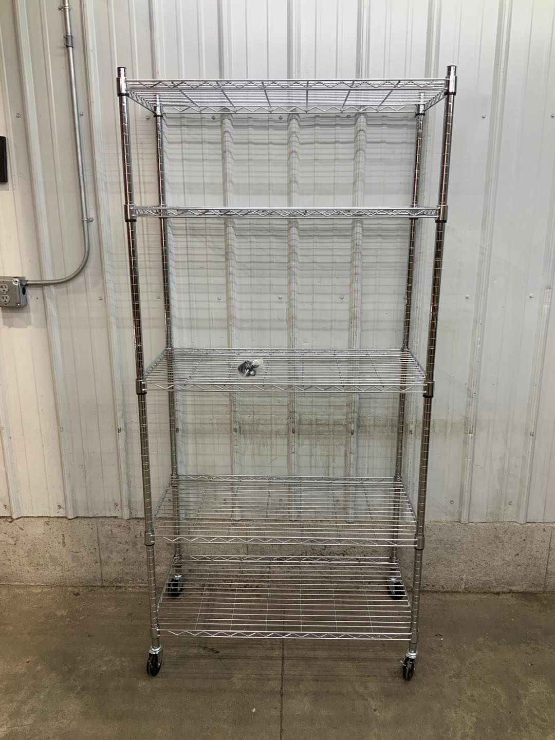 A metal shelf with wheels is sitting in front of a white wall.