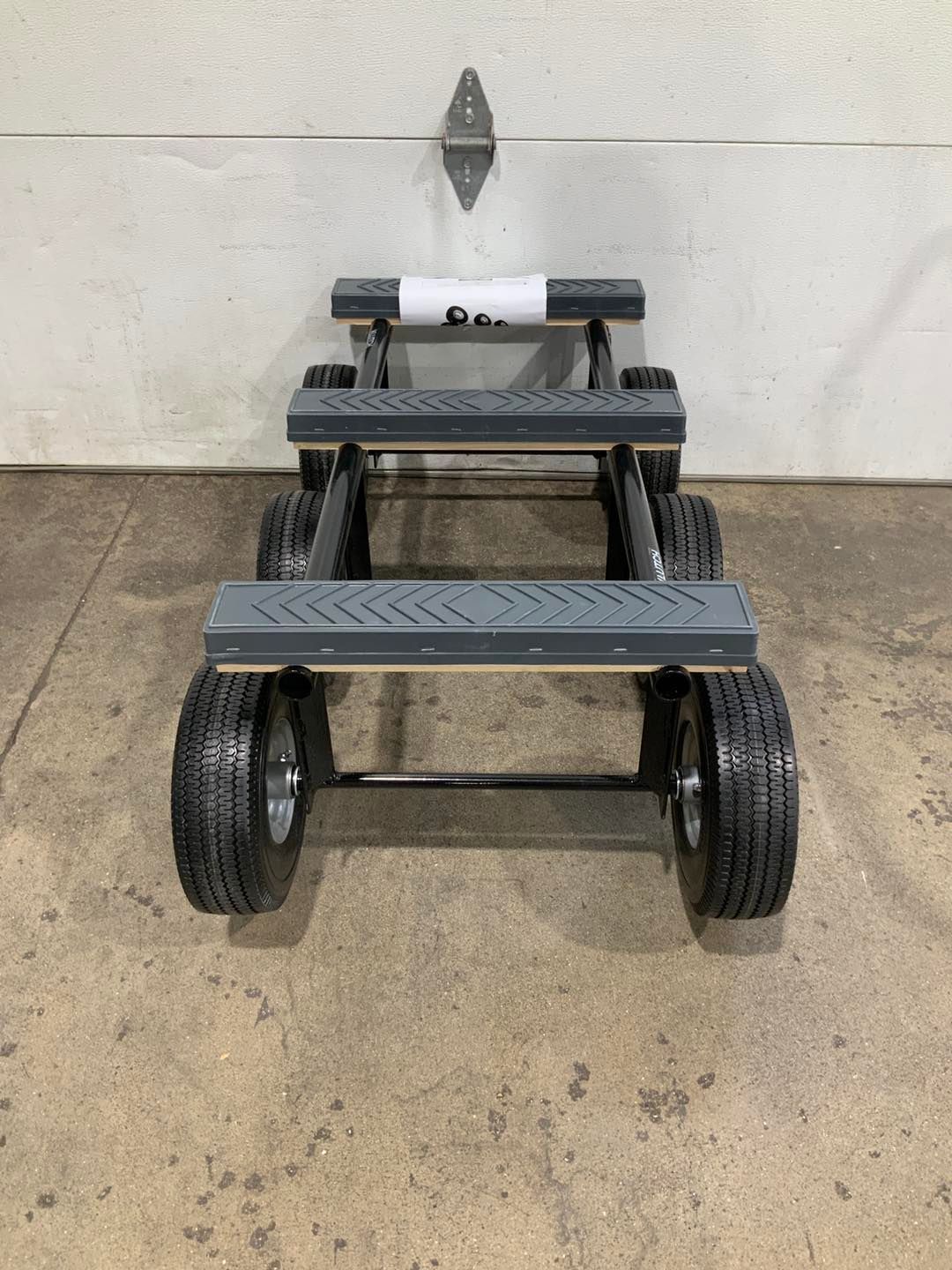 A gray cart with wheels is sitting on a concrete floor in front of a garage door.
