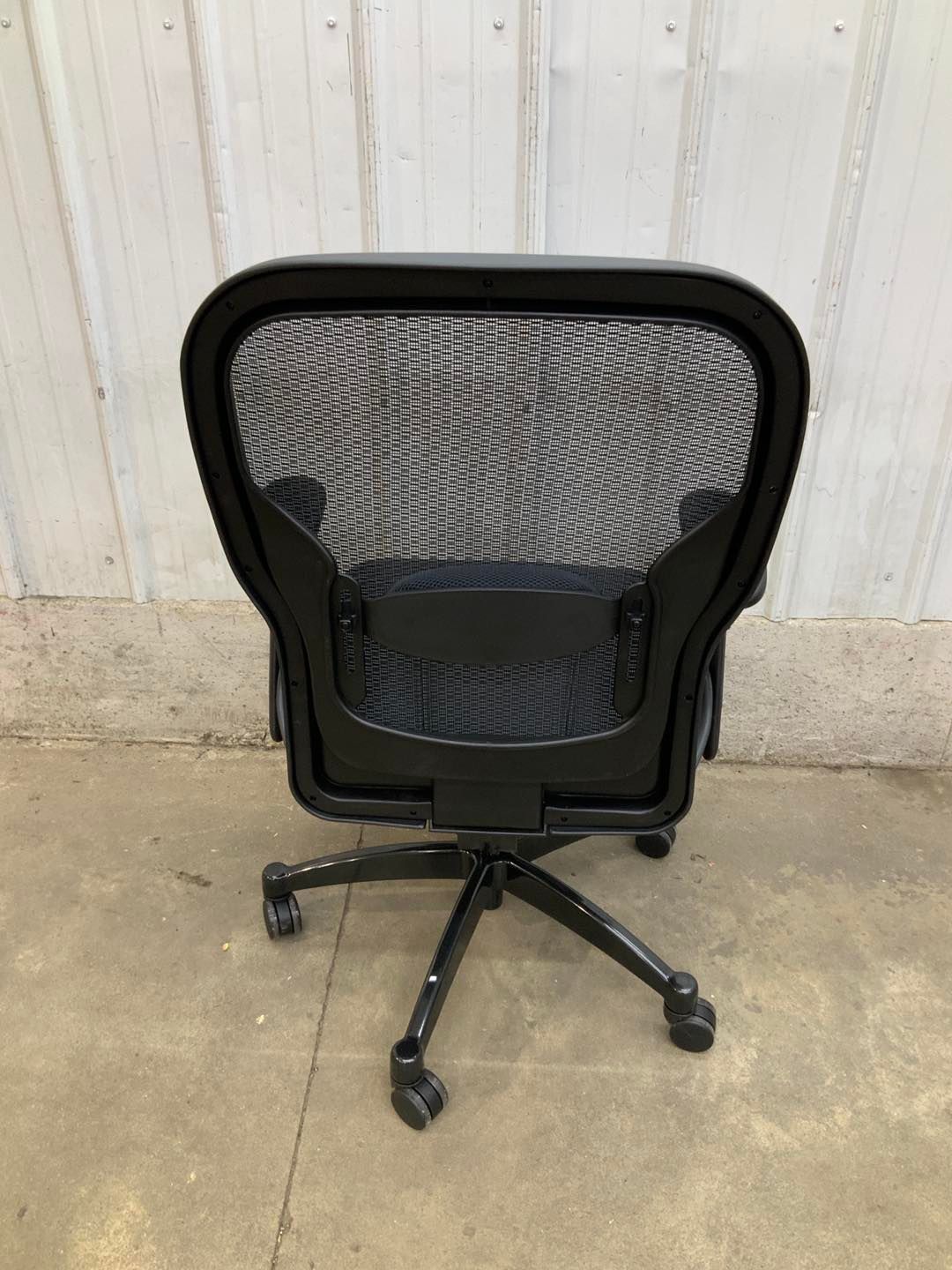 A black mesh office chair with wheels is sitting on a concrete floor.