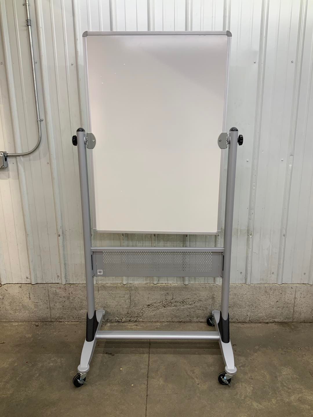 A white board on wheels is sitting on the ground in front of a wall.
