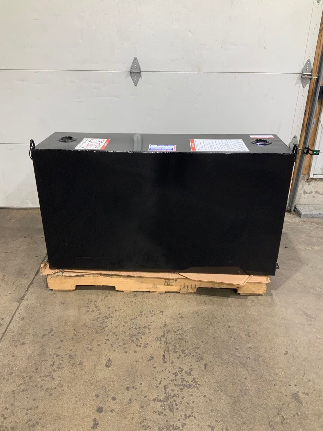 A large black box is sitting on a wooden pallet in front of a garage door.