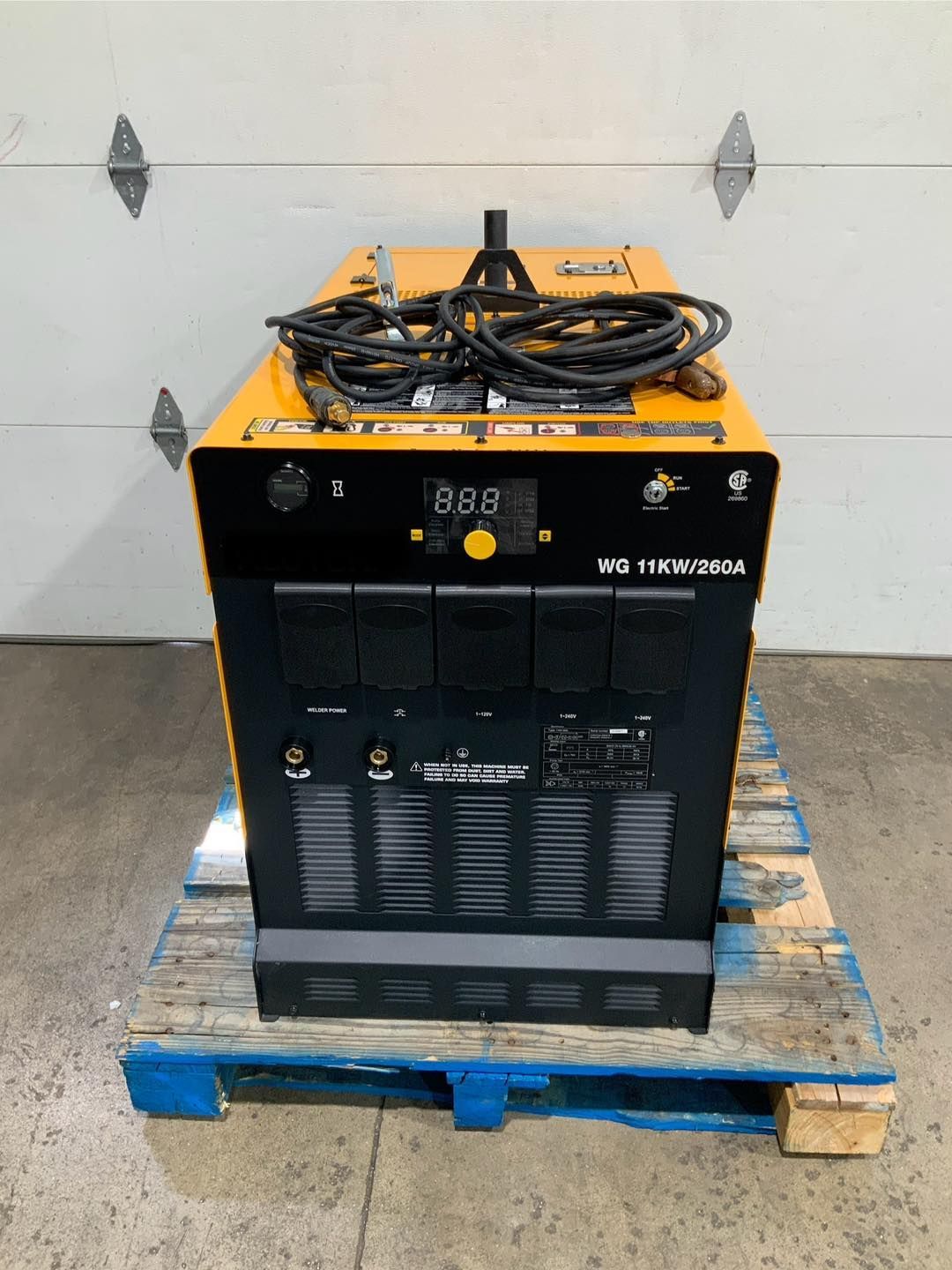 A machine is sitting on a wooden pallet in front of a garage door.