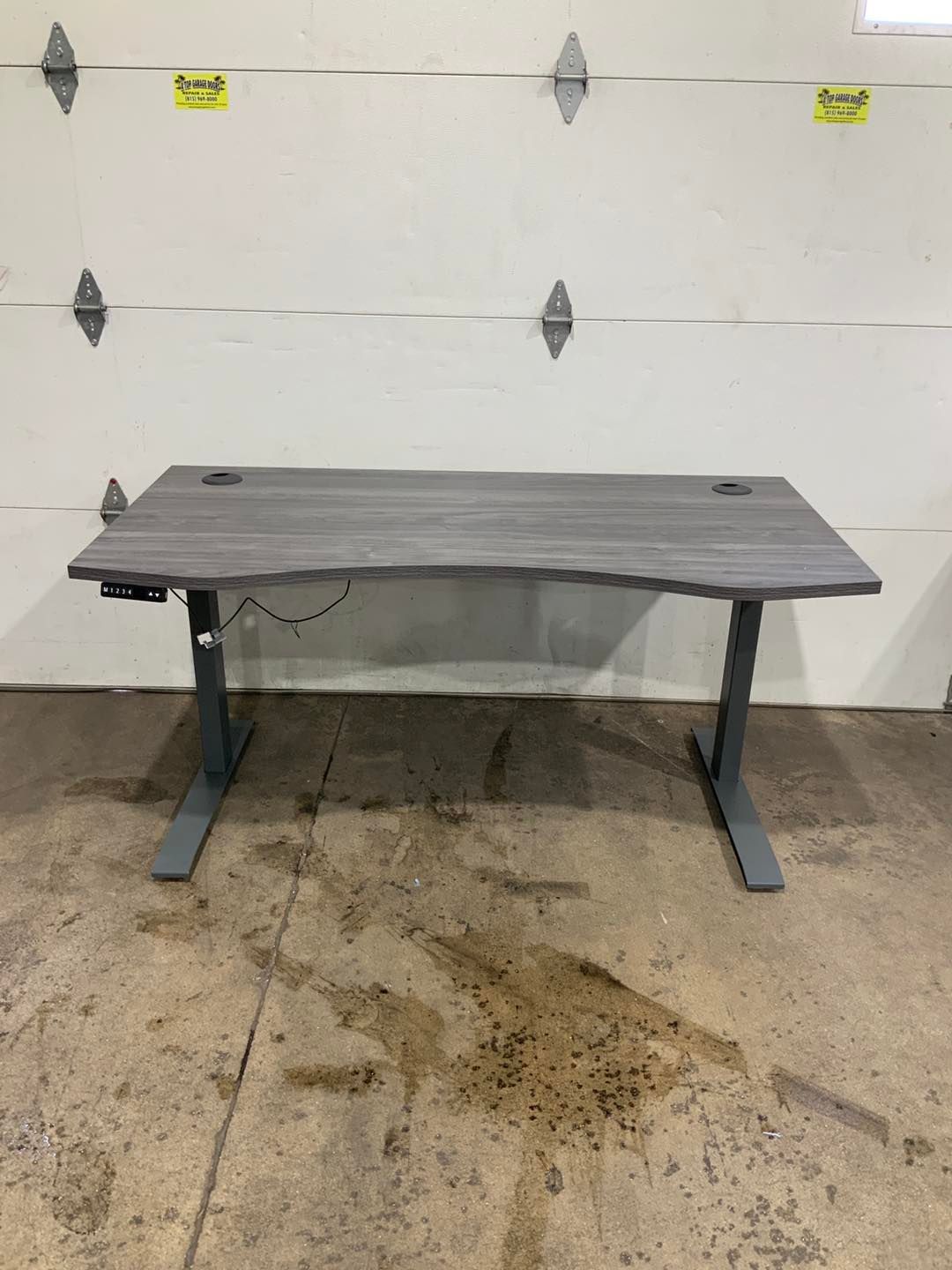 A gray standing desk is sitting in front of a garage door.