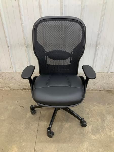 A black office chair is sitting on a concrete floor in front of a white wall.