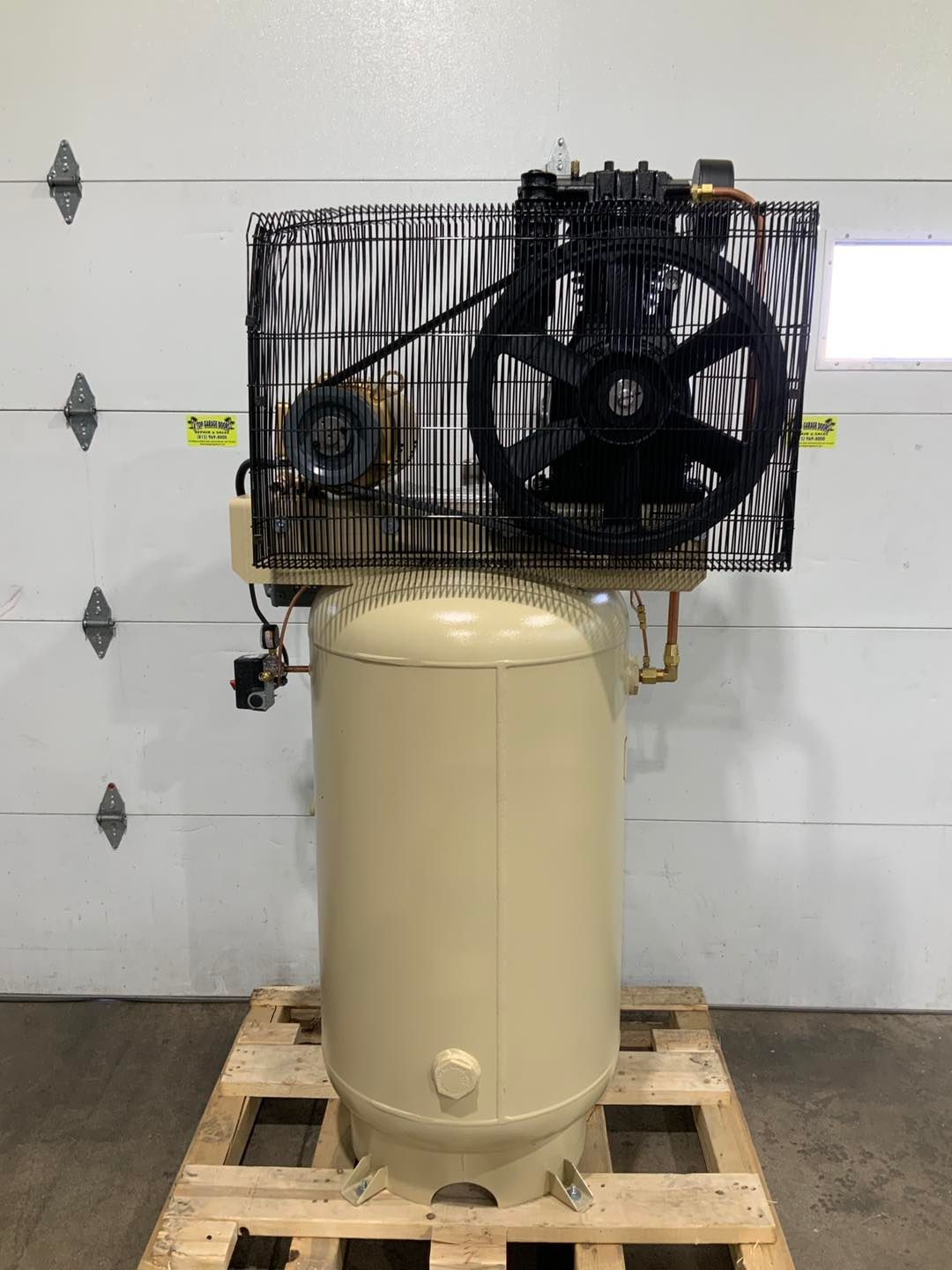 An air compressor is sitting on a wooden pallet in front of a garage door.