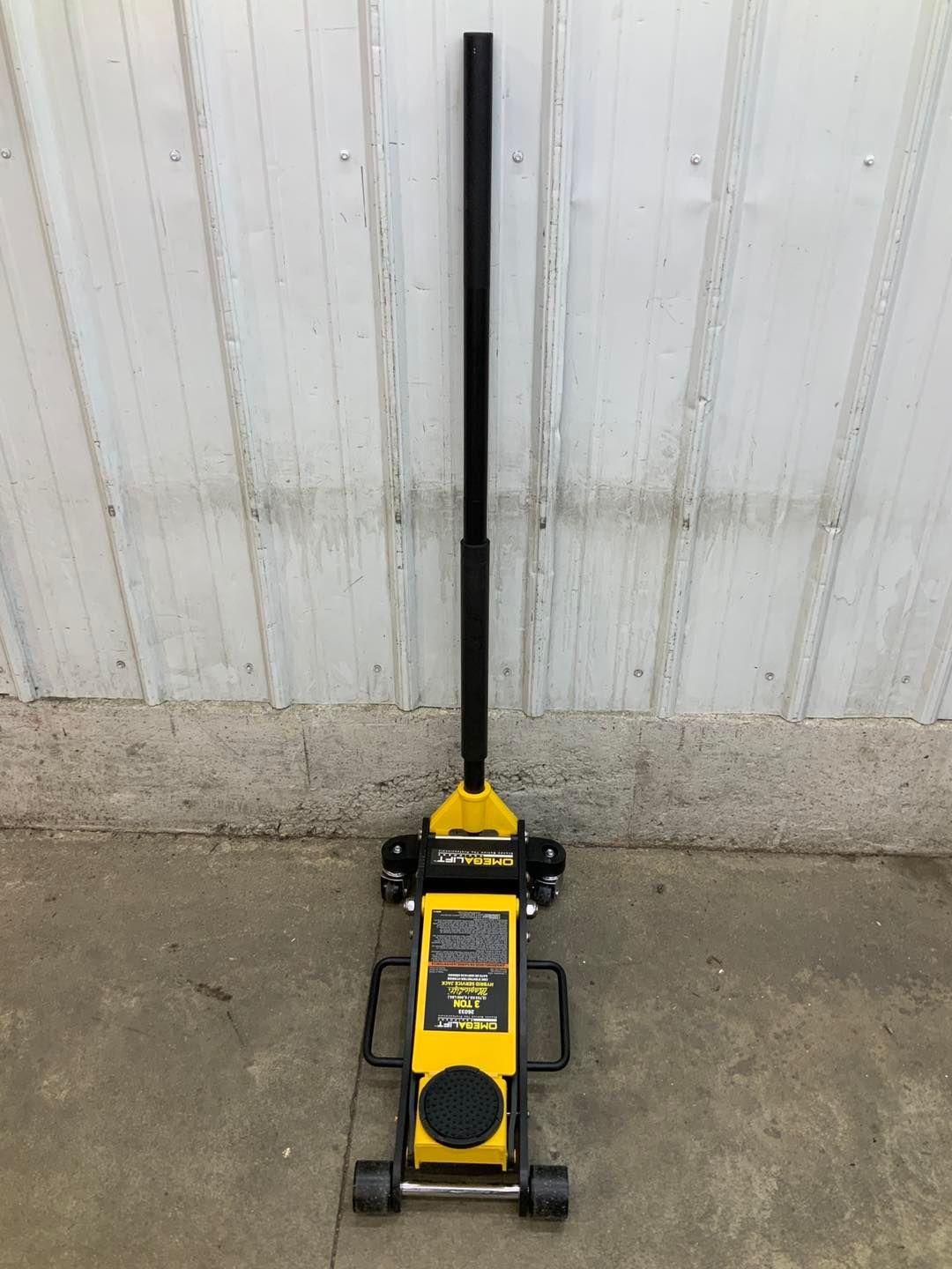 A yellow floor jack with a long handle is sitting on the ground.