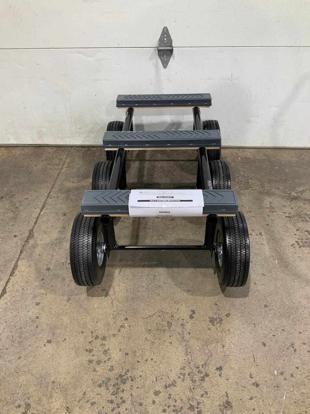A cart with wheels is sitting on the ground in front of a garage door.
