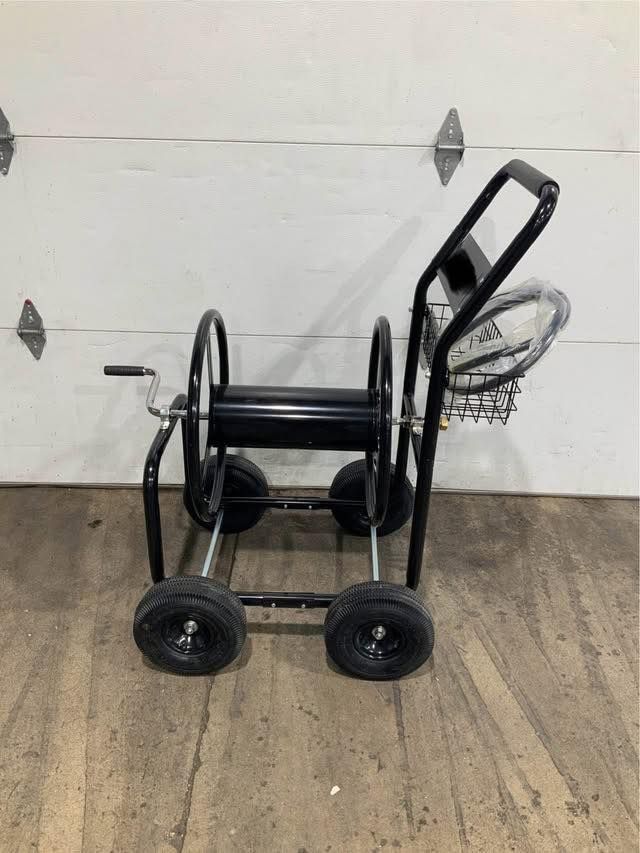 A hose reel on wheels is sitting on a wooden floor in front of a garage door.
