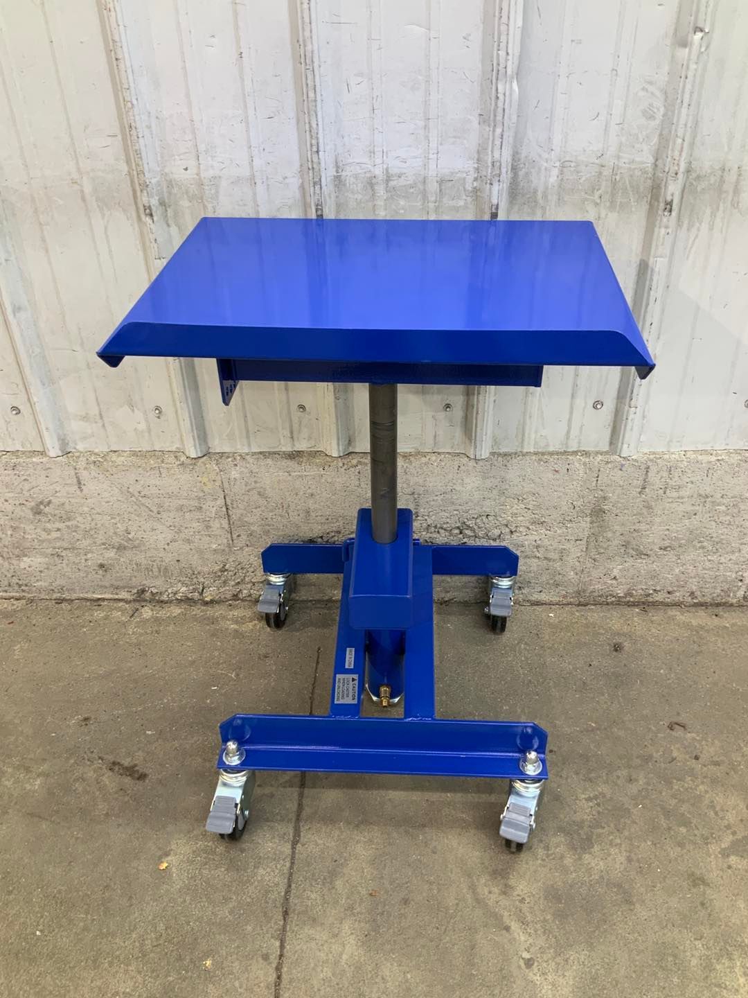 A blue table with wheels is sitting on the ground in front of a white wall.