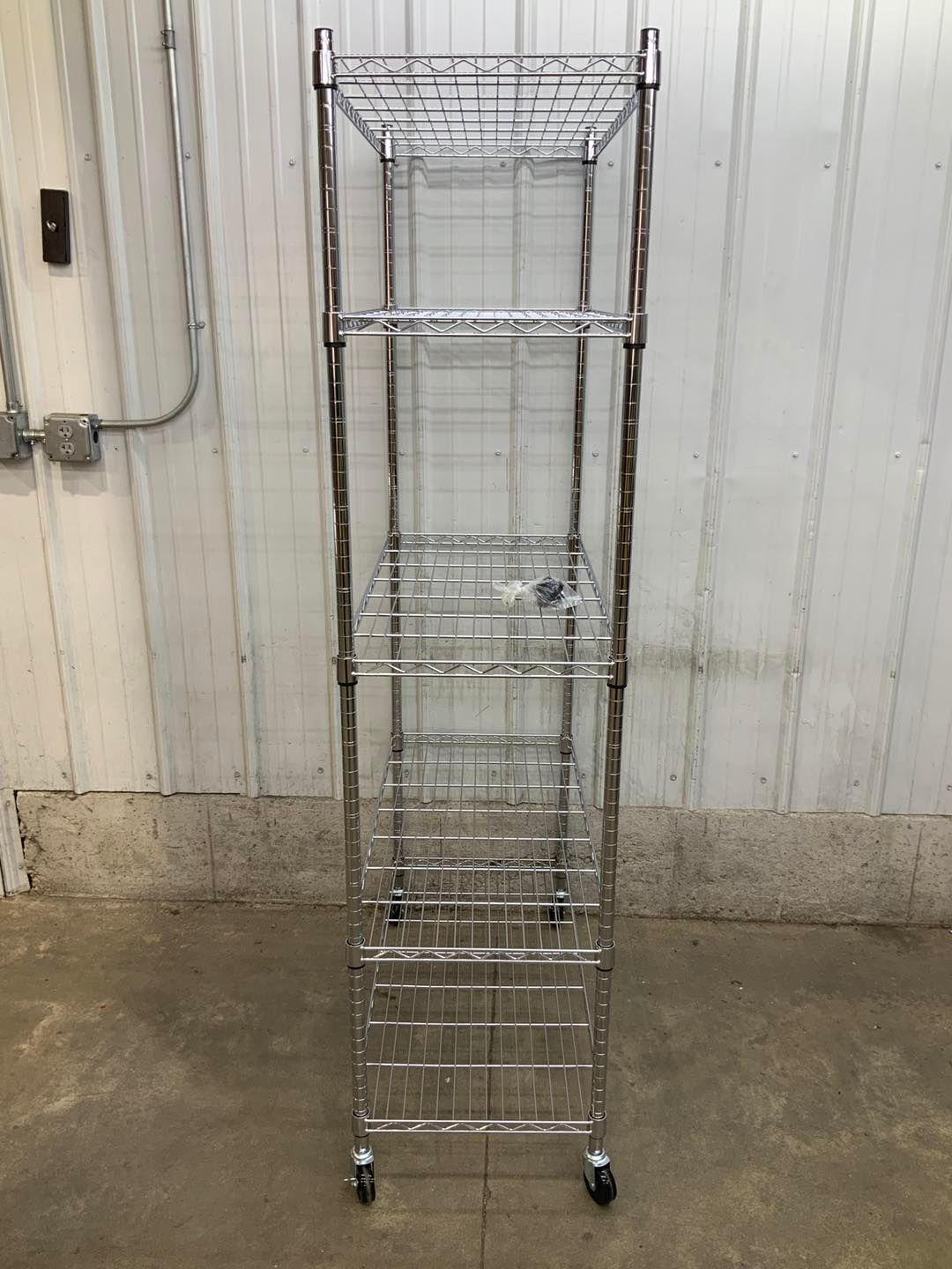 A metal shelf with wheels is sitting on the ground in front of a white wall.