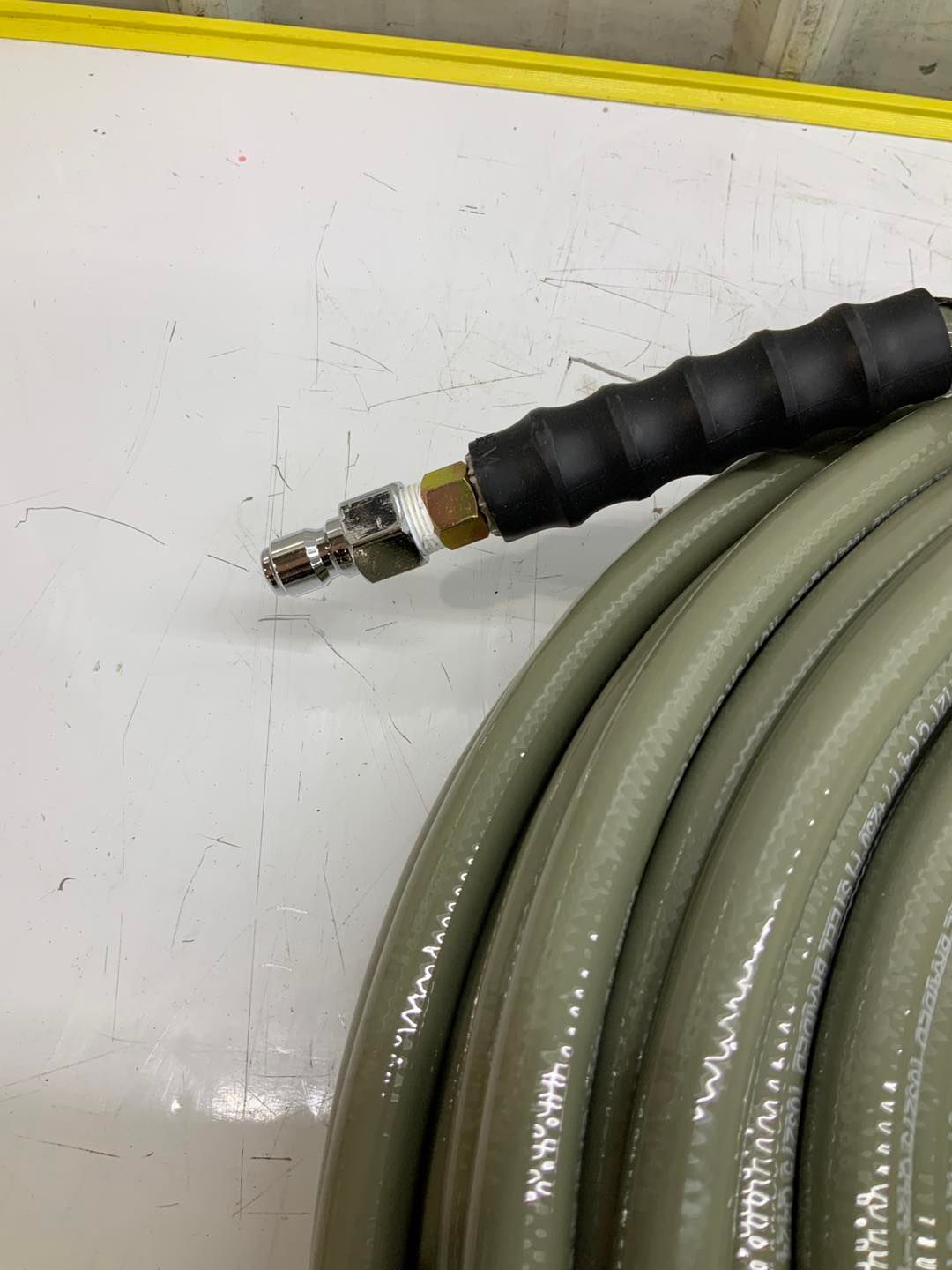 A close up of a hose with a black handle on a white surface.