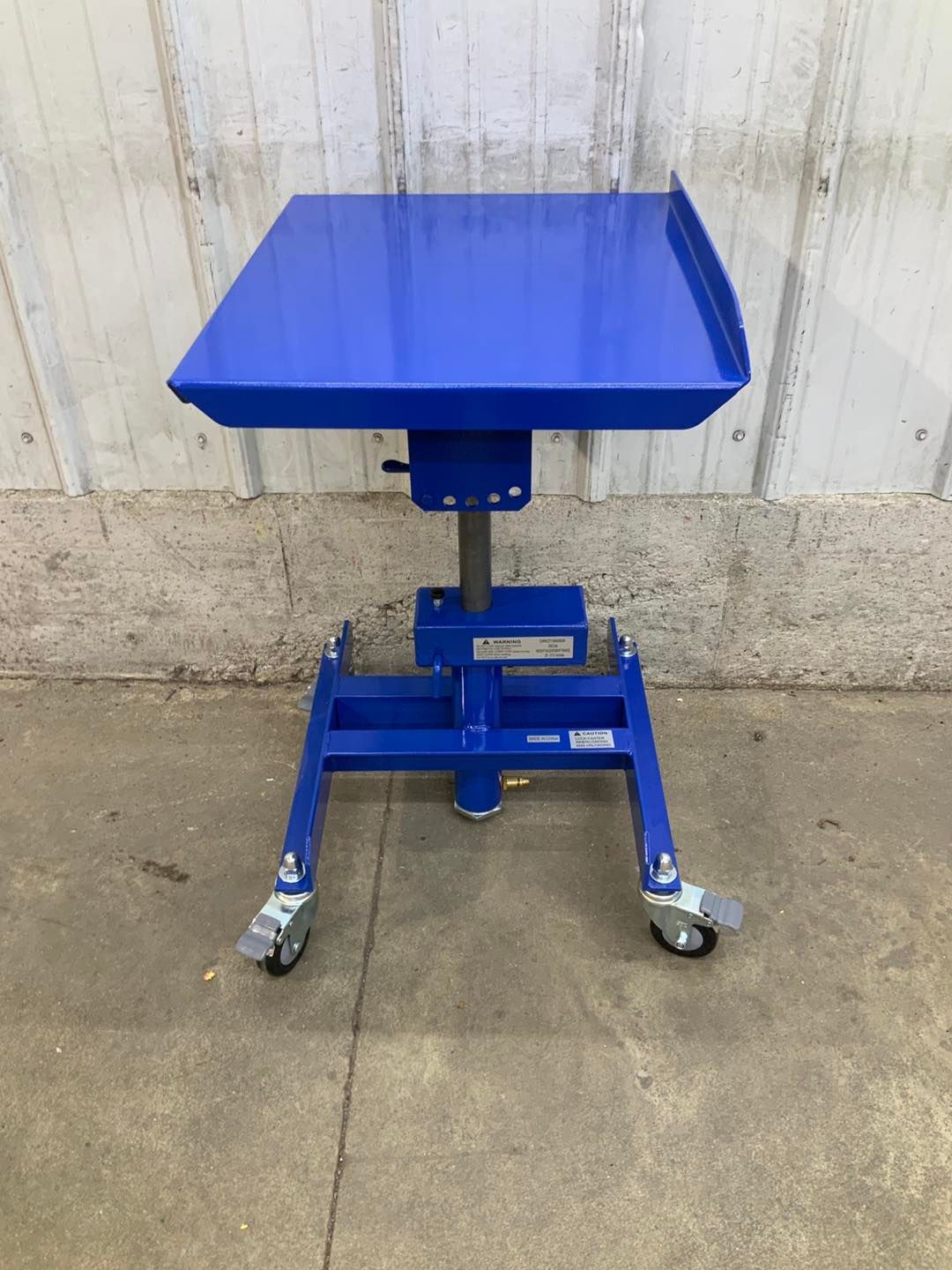 A blue table with wheels is sitting on the ground in front of a white wall.