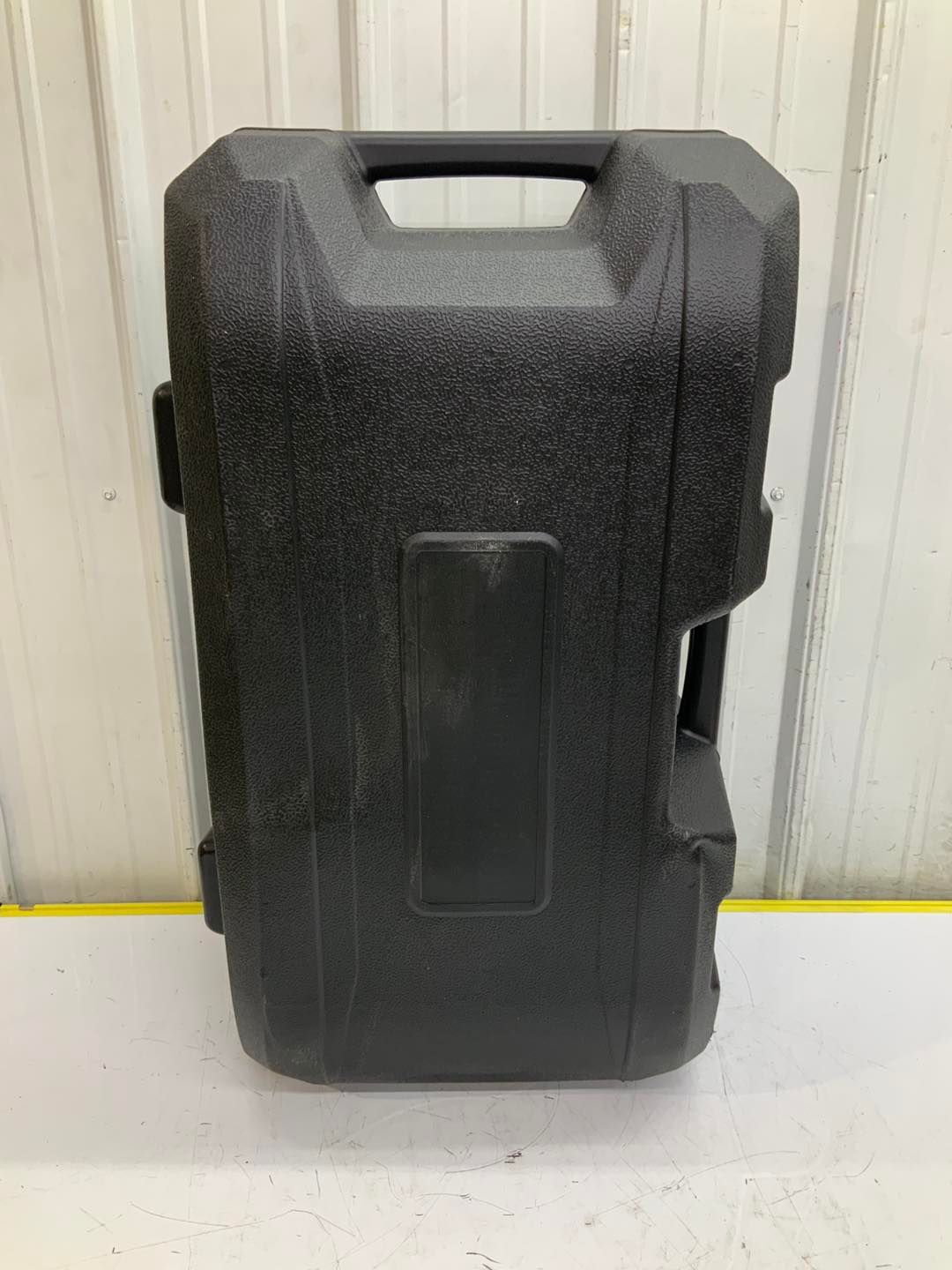 A black plastic case with a handle is sitting on a white table.