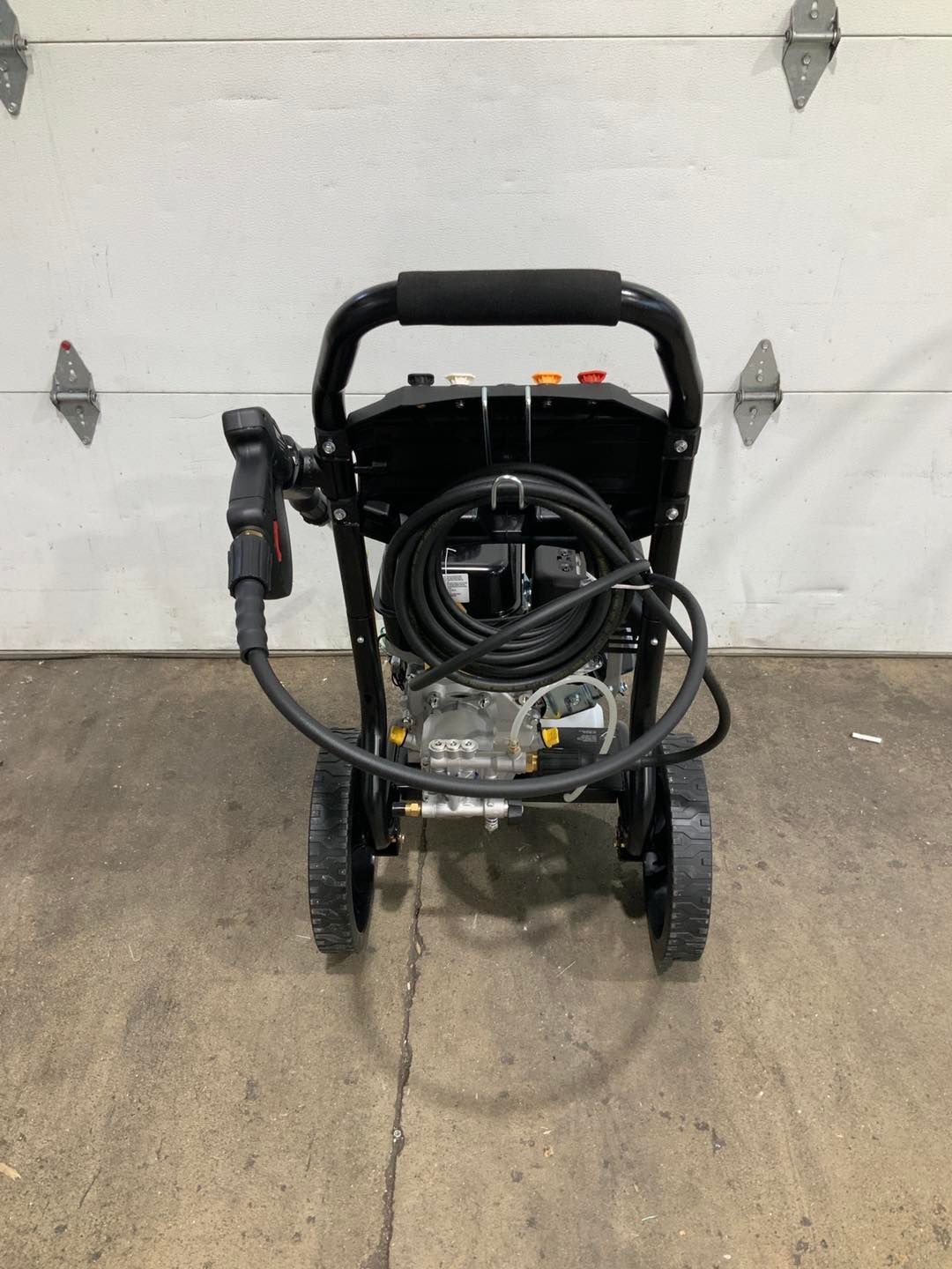A pressure washer is sitting on the ground in front of a garage door.