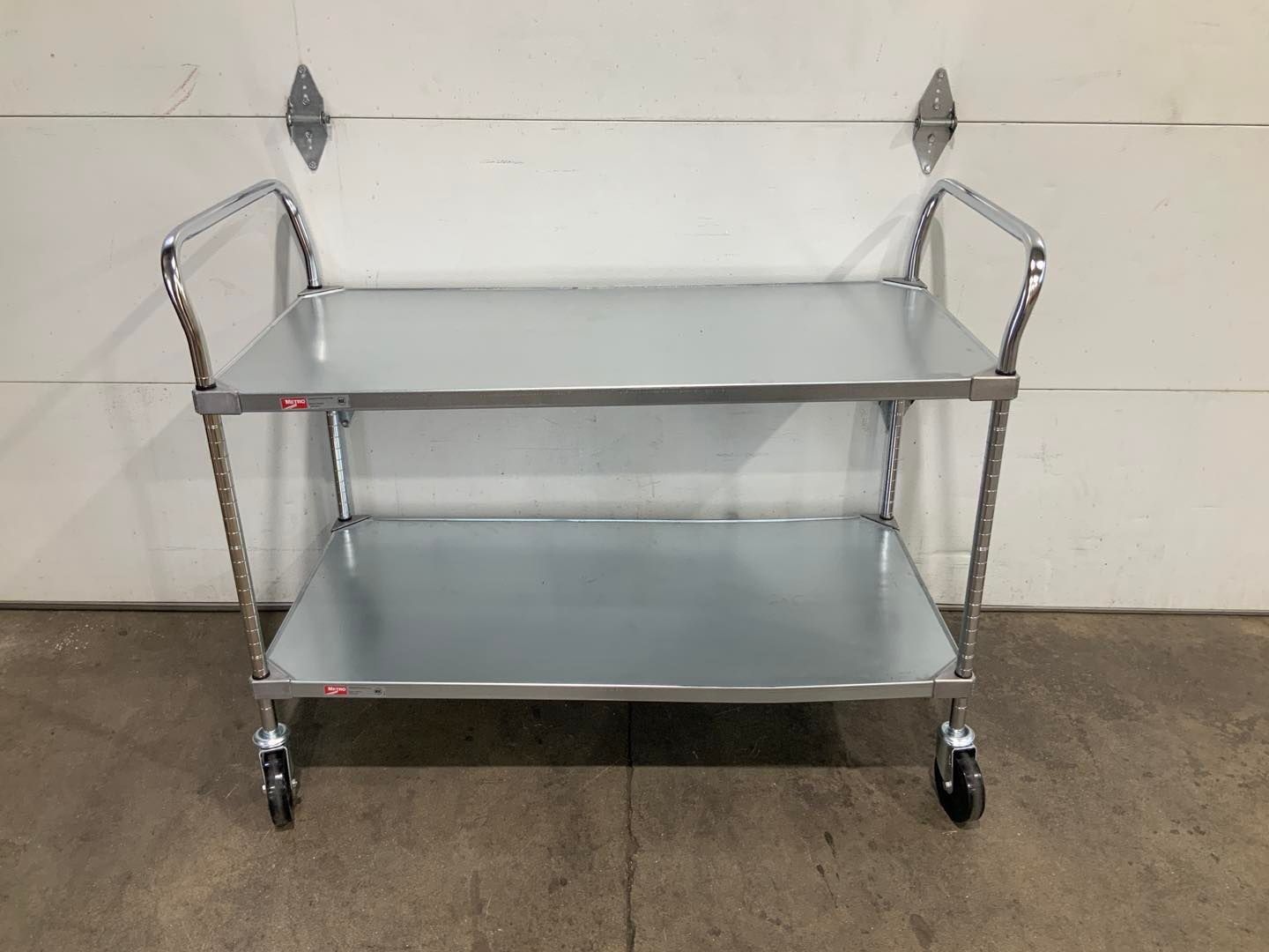 A metal cart with two shelves and wheels is sitting in front of a garage door.