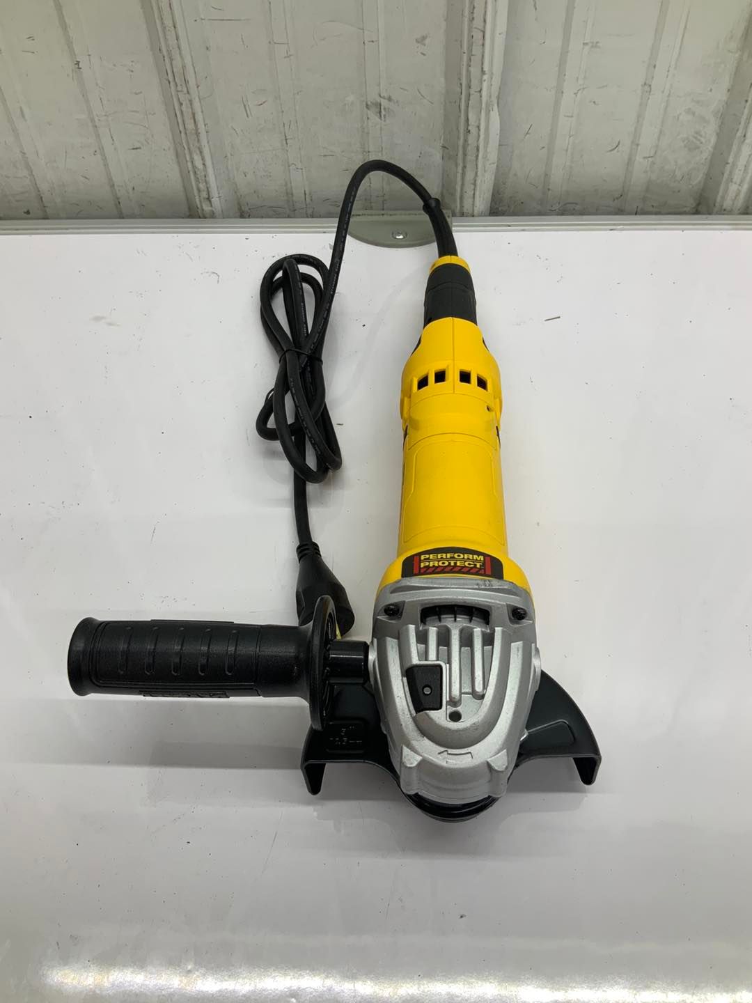 A yellow and black angle grinder is sitting on top of a white table.