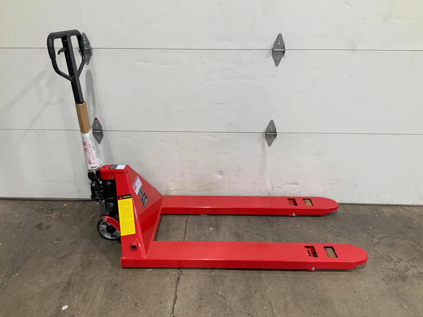 A red pallet truck is sitting in front of a garage door.