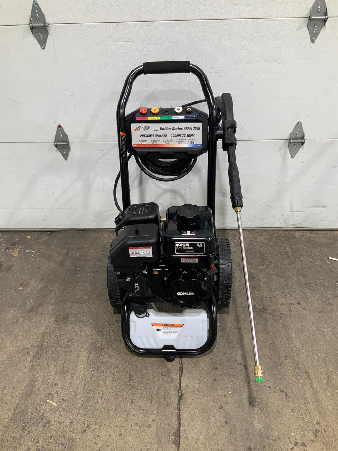A gas powered pressure washer is sitting in front of a garage door.