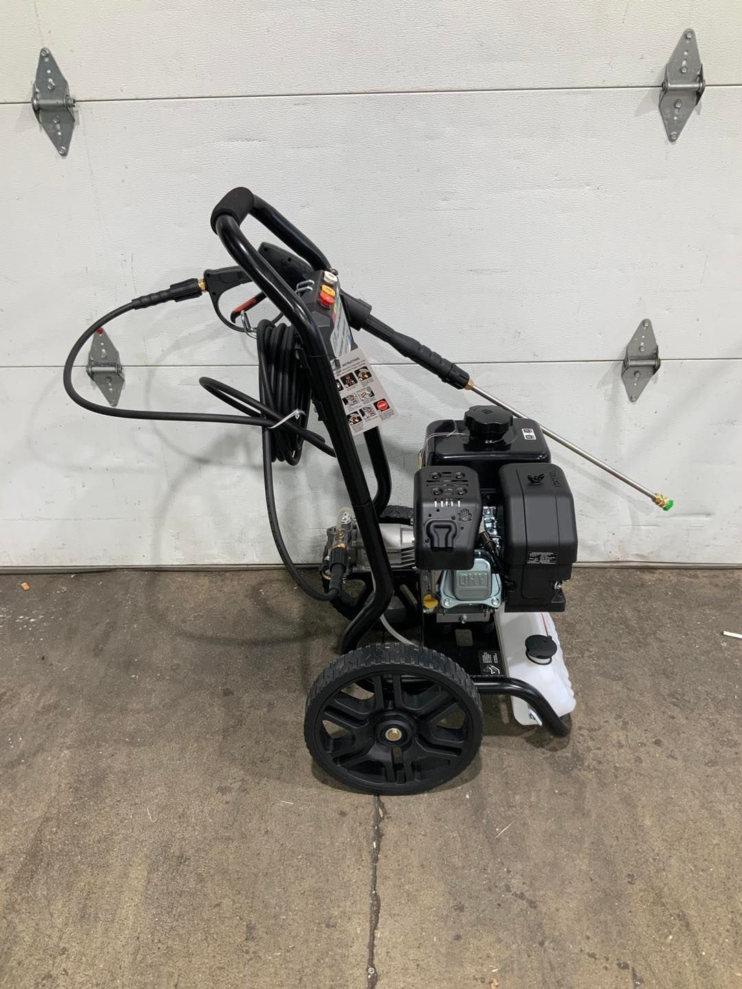A gas powered pressure washer is sitting in front of a garage door.