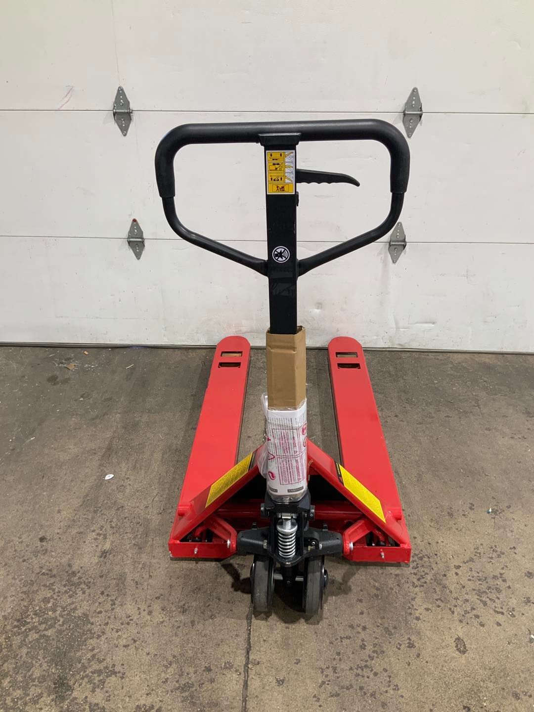 A red pallet truck is sitting in front of a garage door.