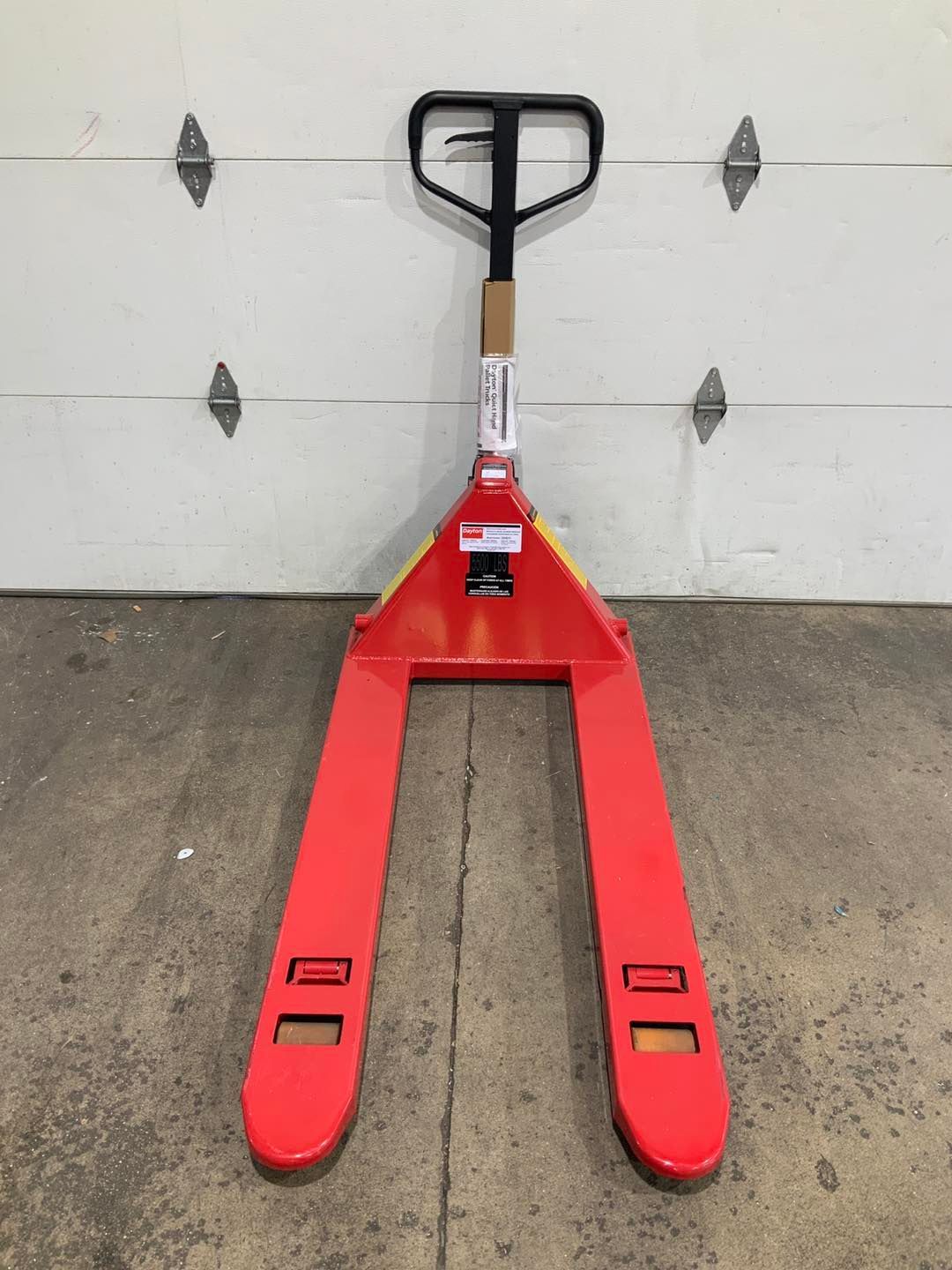 A red pallet truck is sitting in front of a garage door.