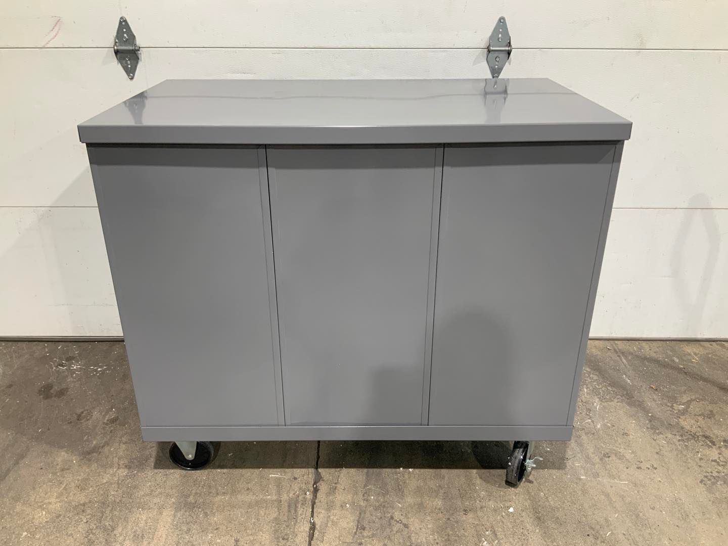 A gray cabinet with wheels is sitting on the ground in front of a garage door.