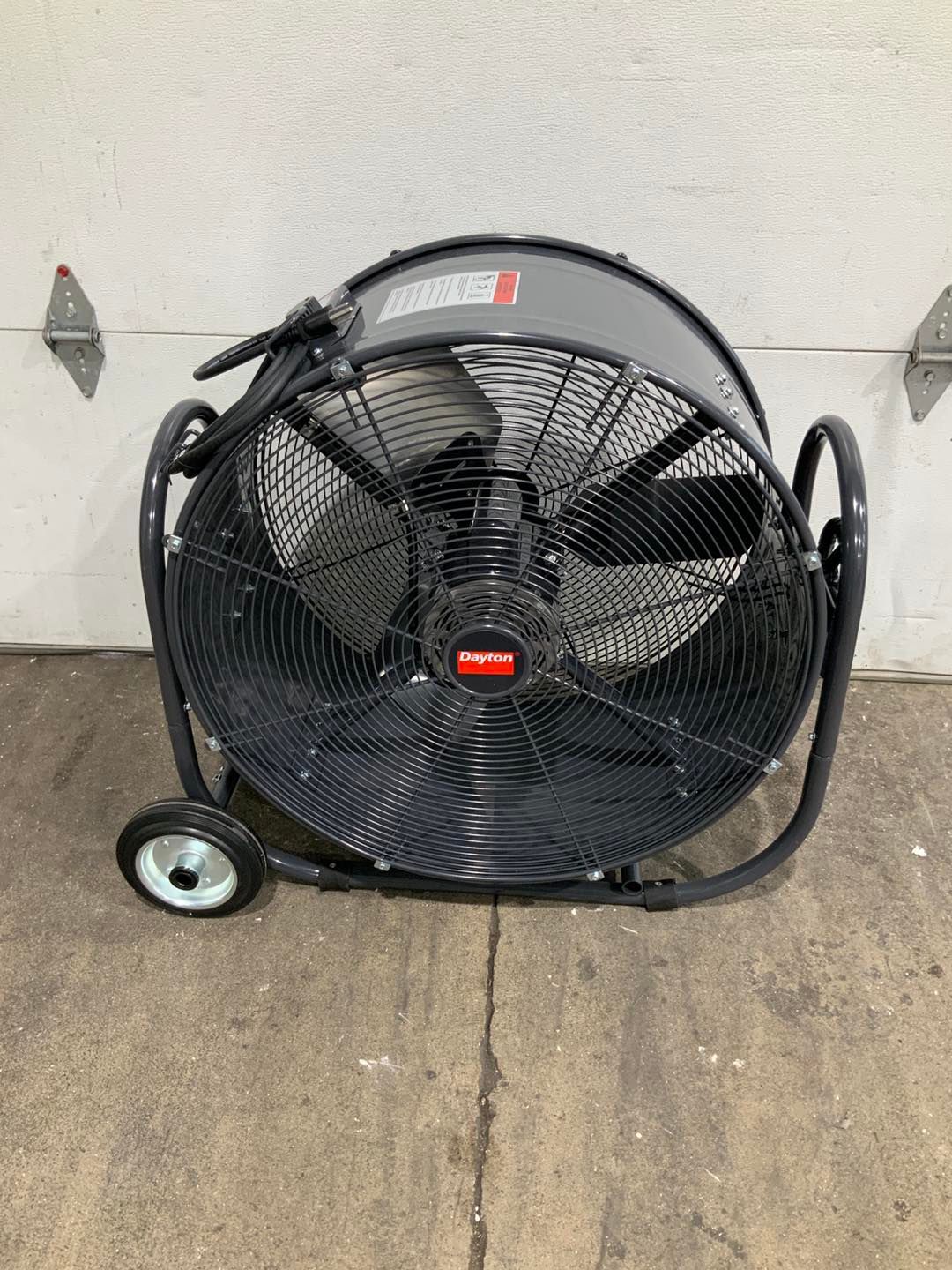 A large fan with wheels is sitting on the ground in front of a garage door.