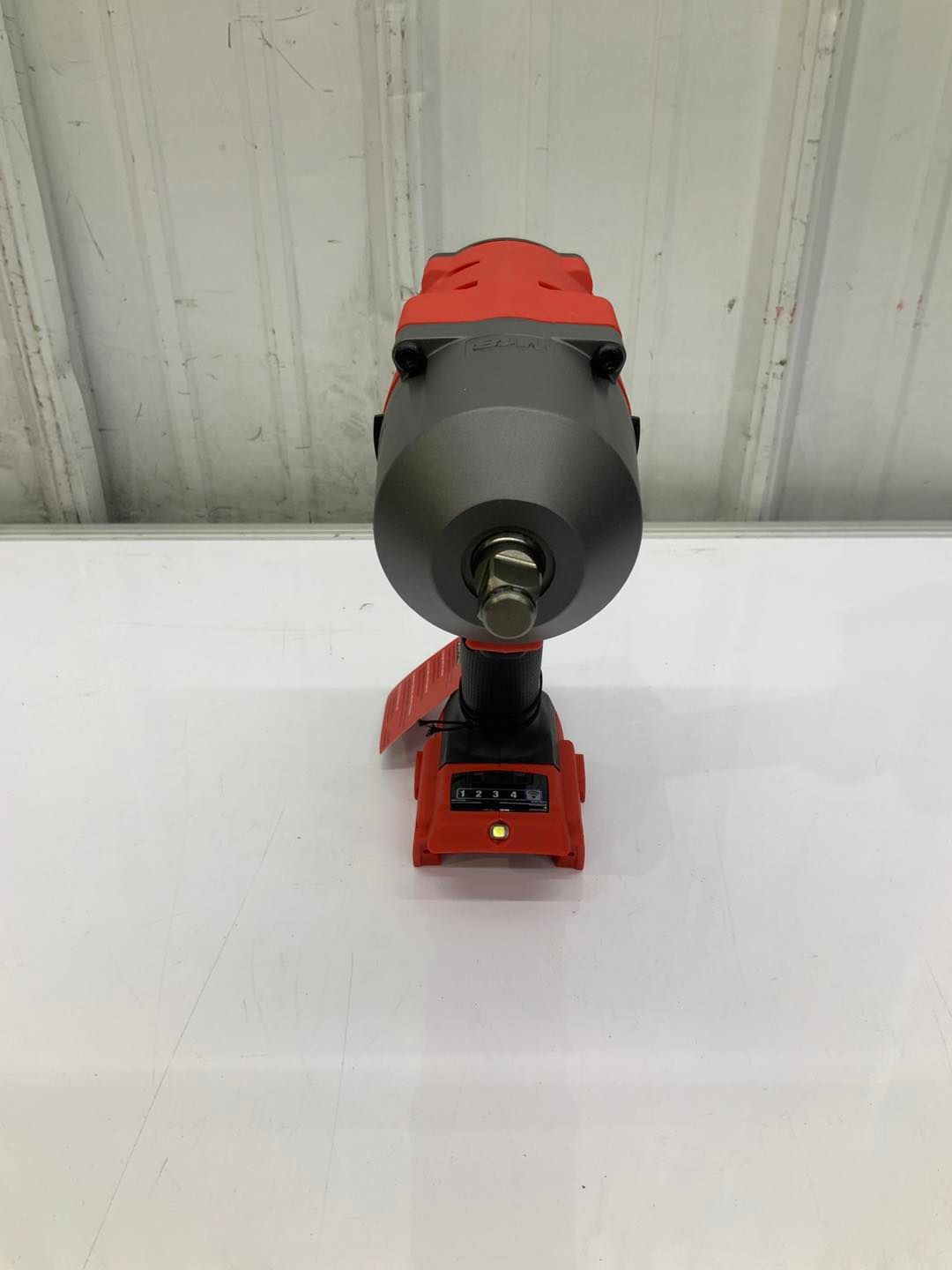 A red and black cordless impact wrench is sitting on a white table.