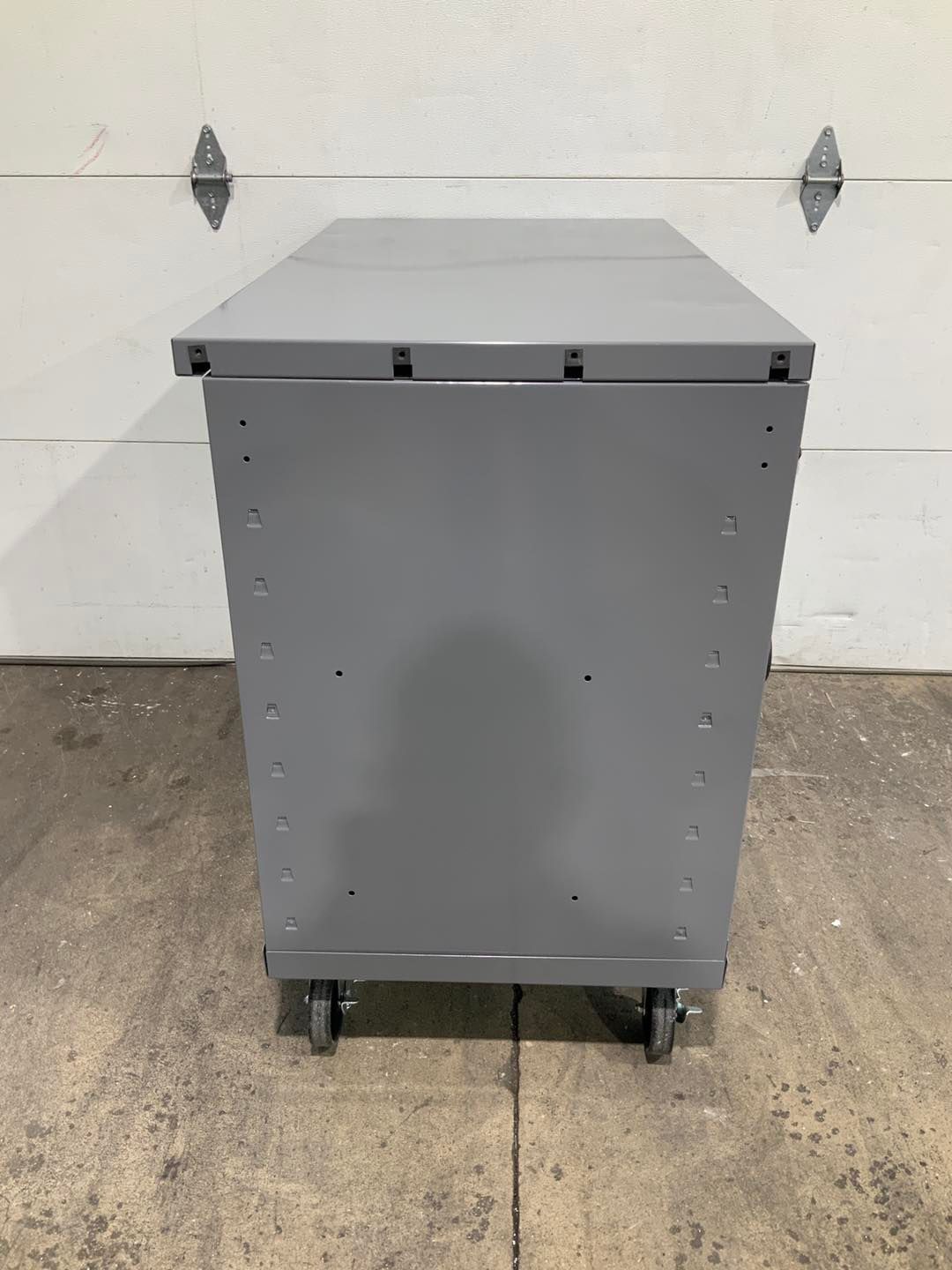 A gray metal cabinet with wheels is sitting in front of a garage door.