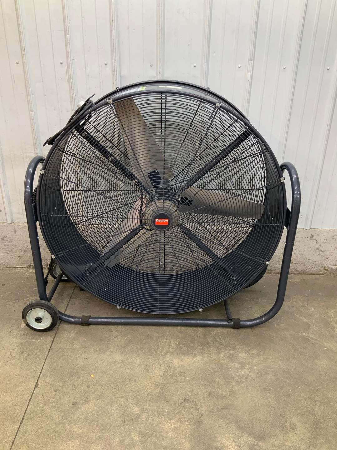 A large fan with wheels is sitting on the ground in front of a white wall.