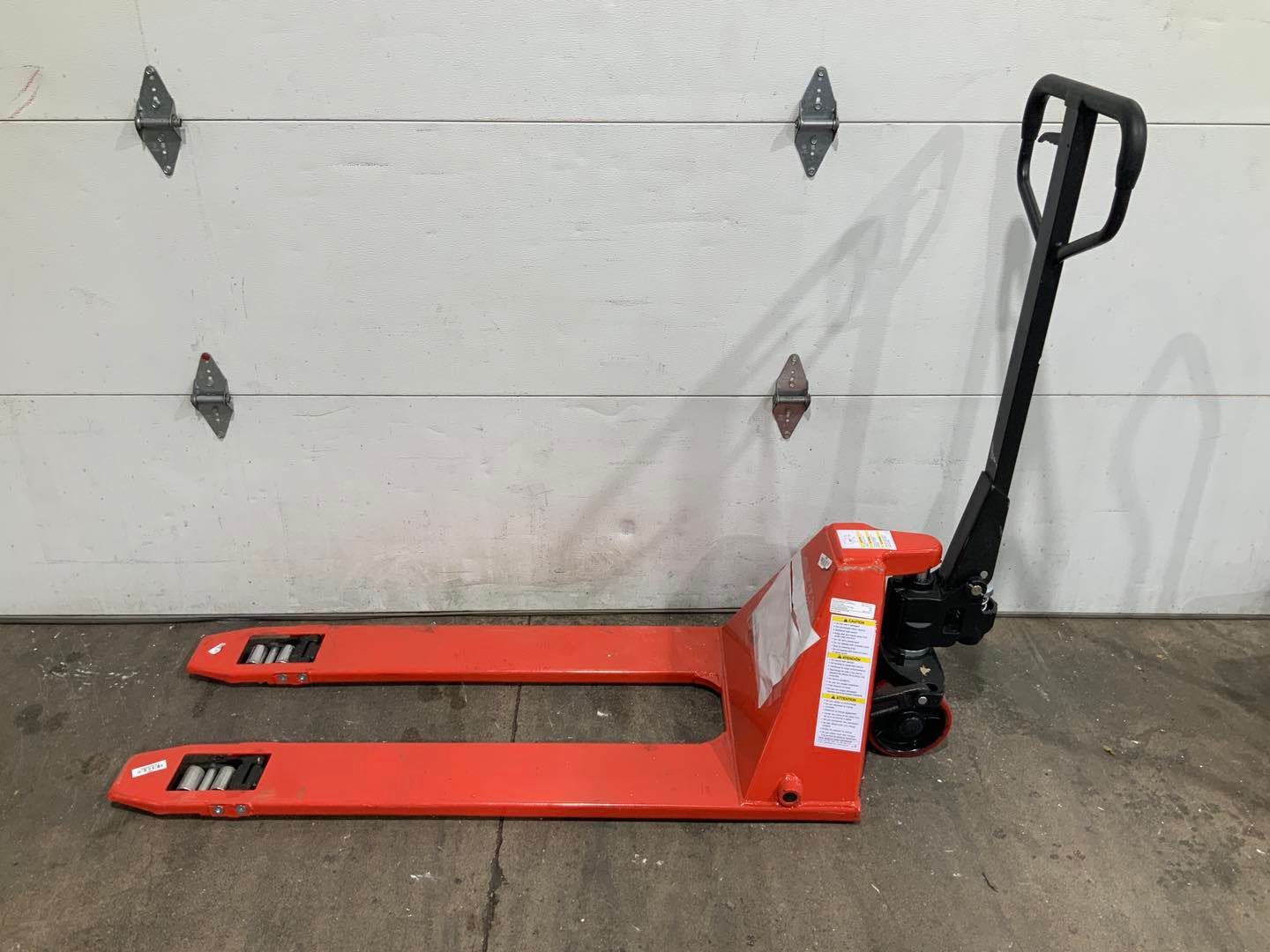 A red pallet truck is sitting in front of a garage door.