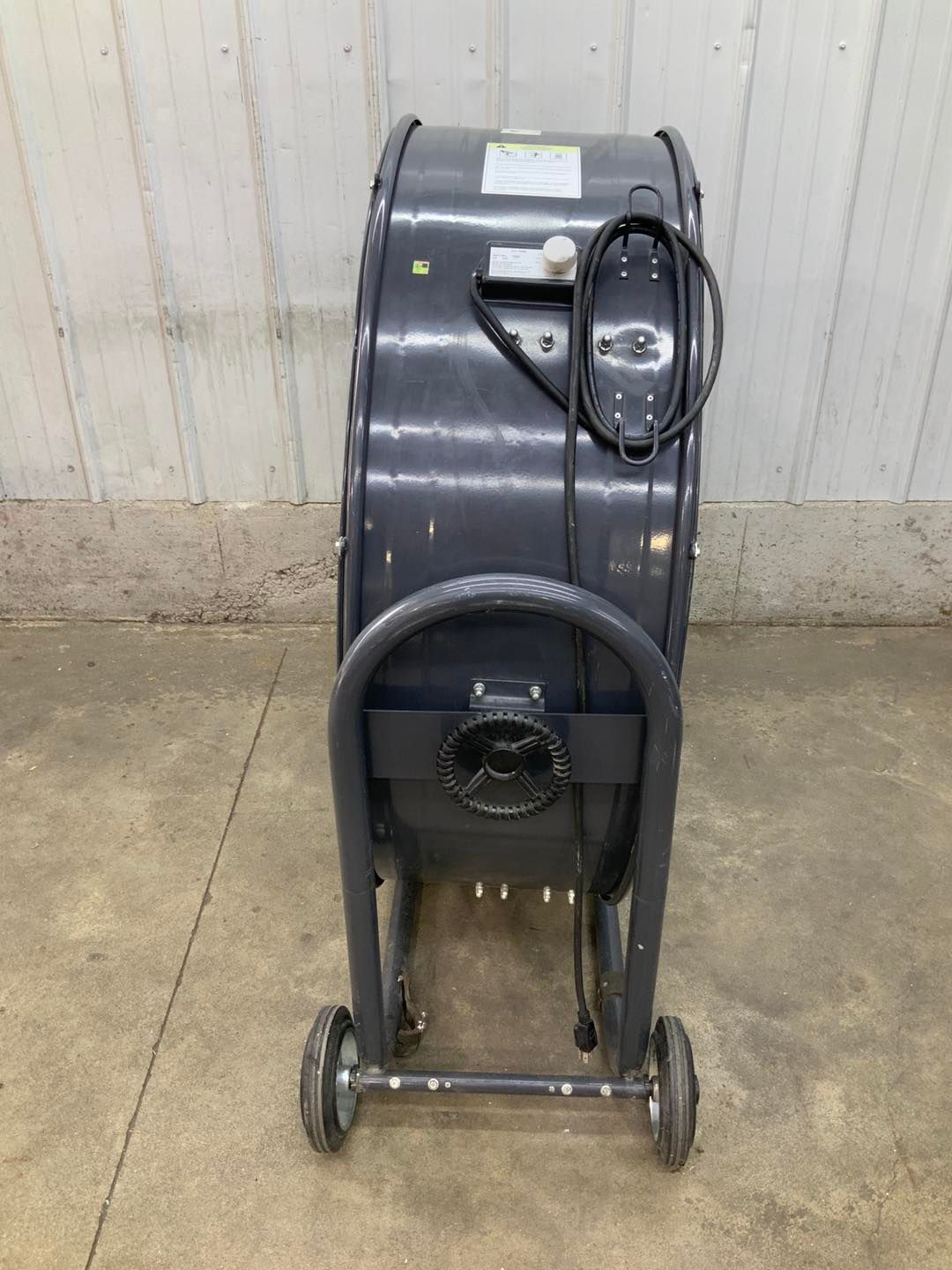 A large fan with wheels is sitting on a concrete floor.