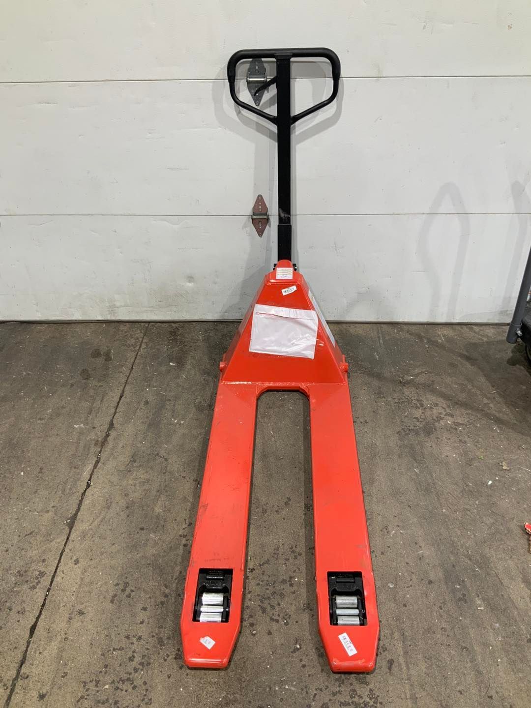A red pallet truck is sitting in front of a garage door.