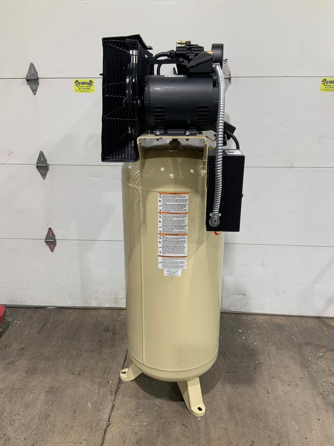 A large air compressor is sitting in front of a garage door.