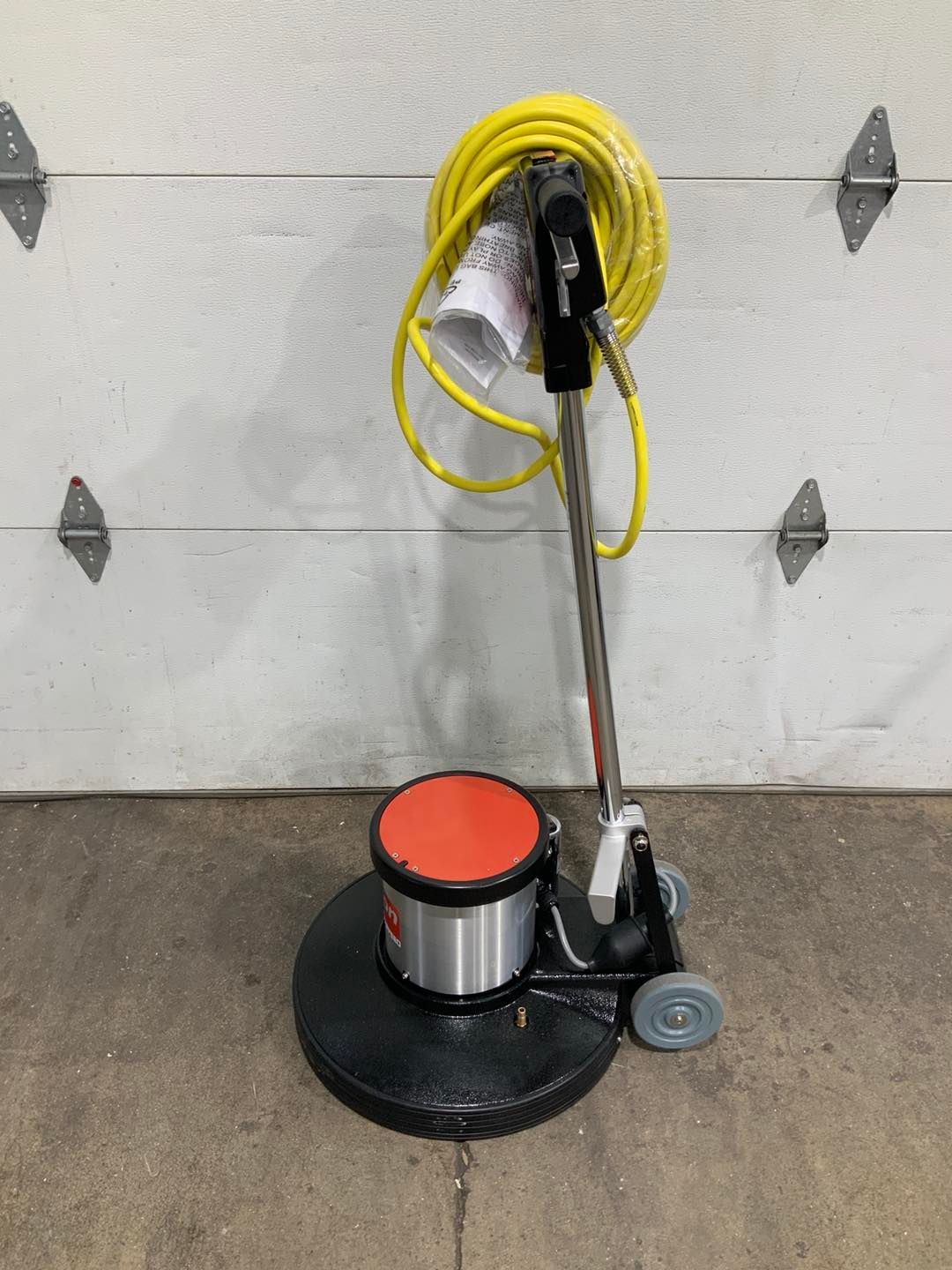 A vacuum cleaner with a yellow cord attached to it is sitting in front of a garage door.
