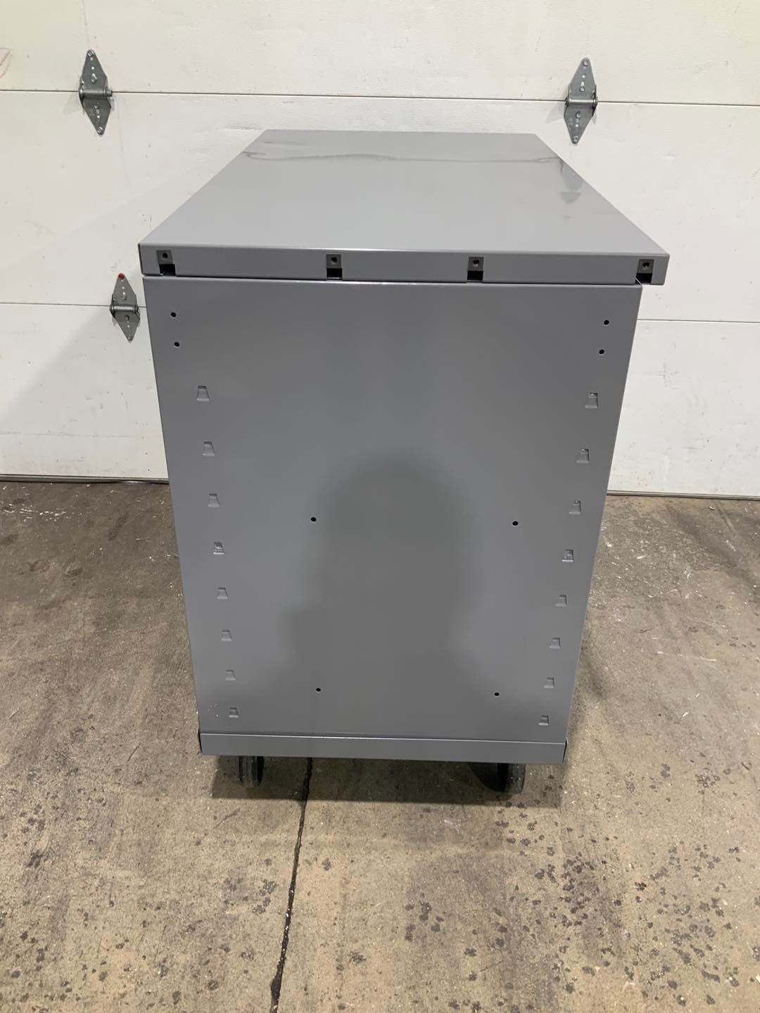 A gray metal box is sitting on the ground in front of a garage door.