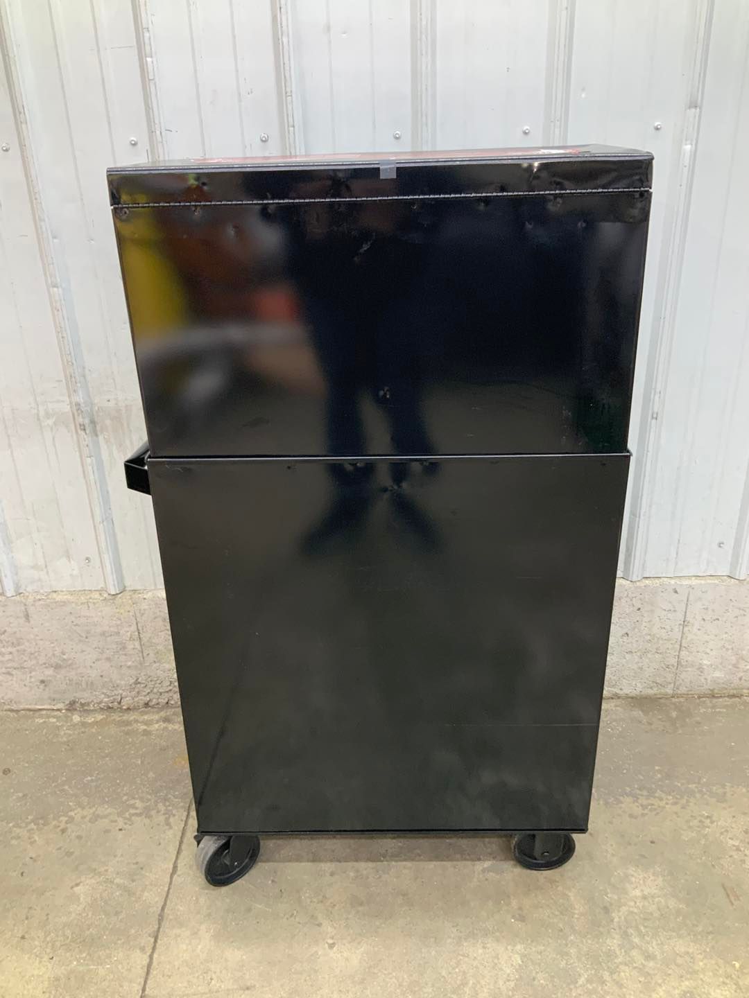 A black cabinet with wheels is sitting on the ground in front of a white wall.