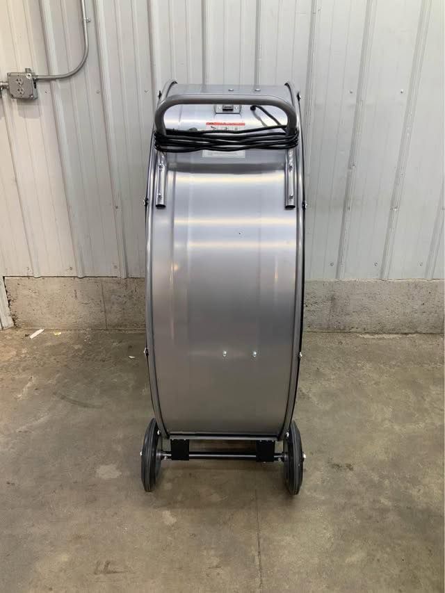 A stainless steel fan with wheels is sitting on the ground in front of a building.